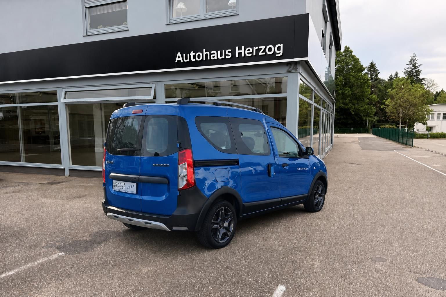 Blauer Dacia Dokker Stepway Van - Seitenansicht von hinten rechts vor Autohaus Herzog