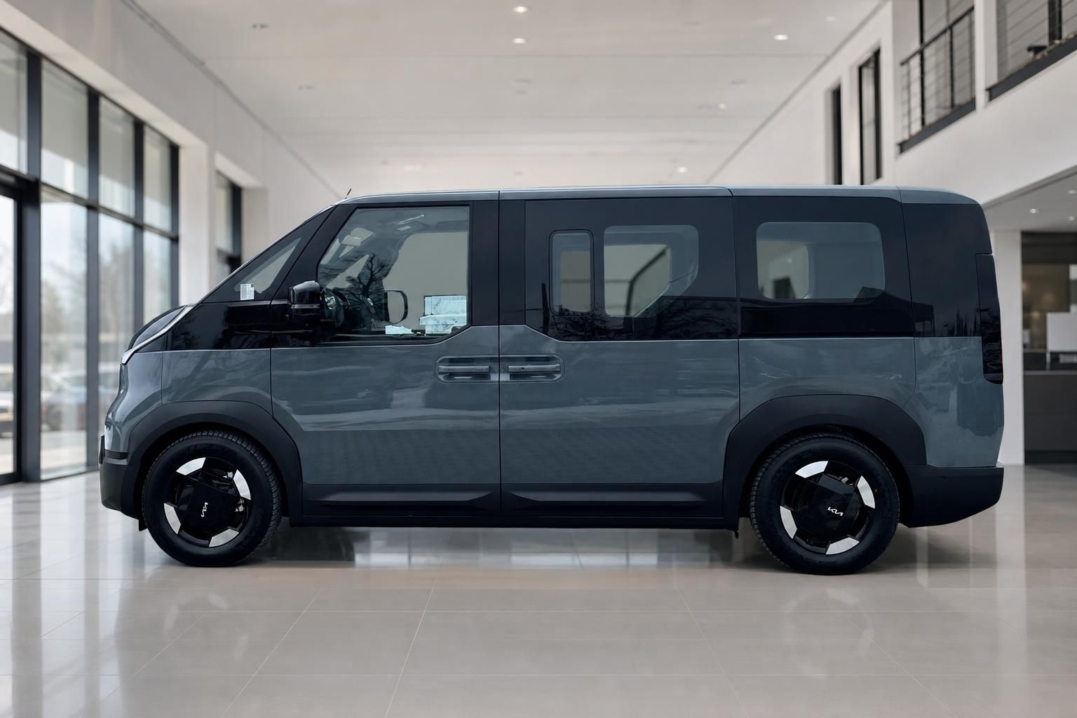 Kia PV5 Passenger Van, Seitenansicht in Grau im Showroom