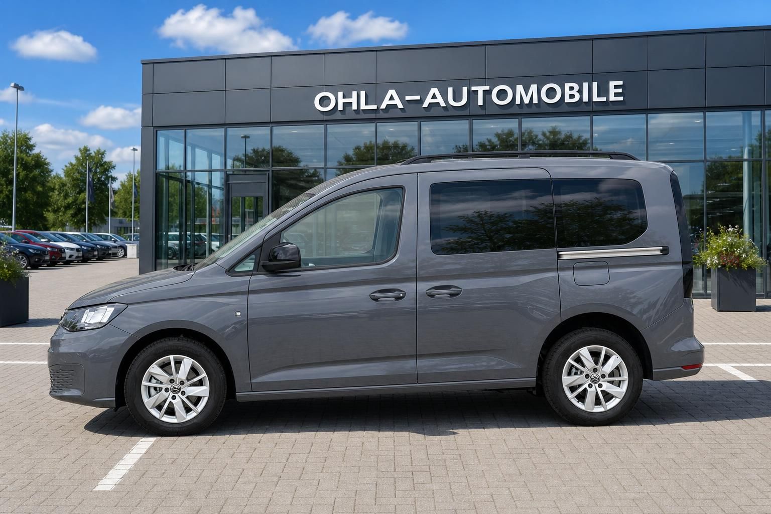 VW Caddy grau Seitenansicht vor moderner Autohausfassade