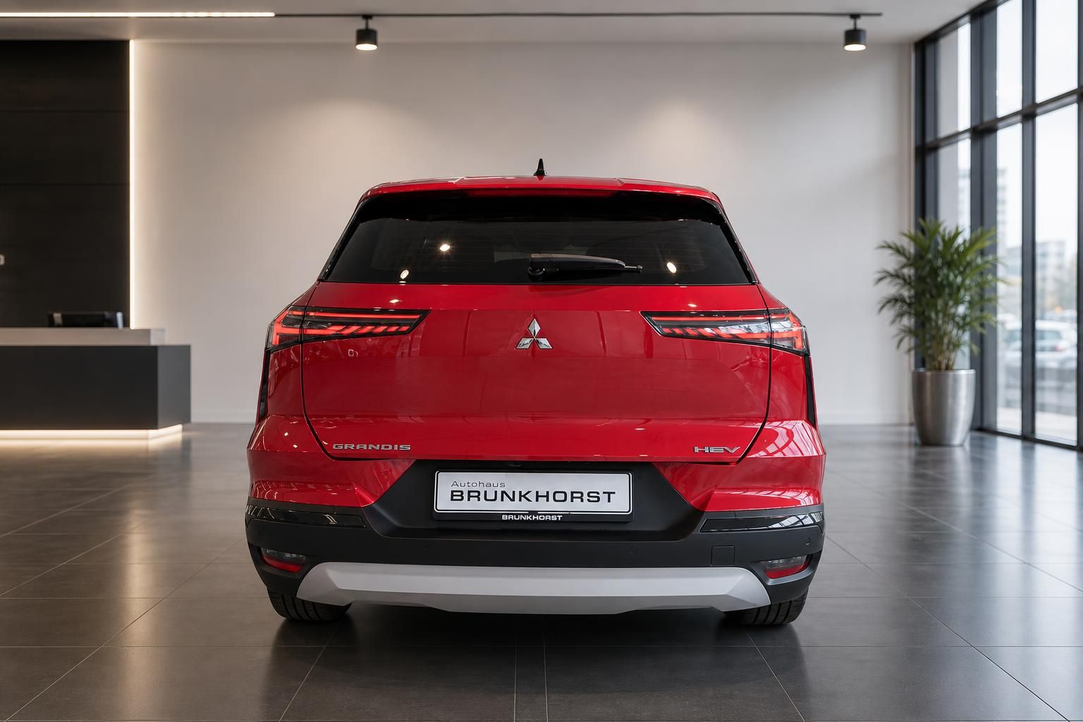 Heckansicht roter Mitsubishi Grandis HEV Hybrid-SUV in elegantem Showroom