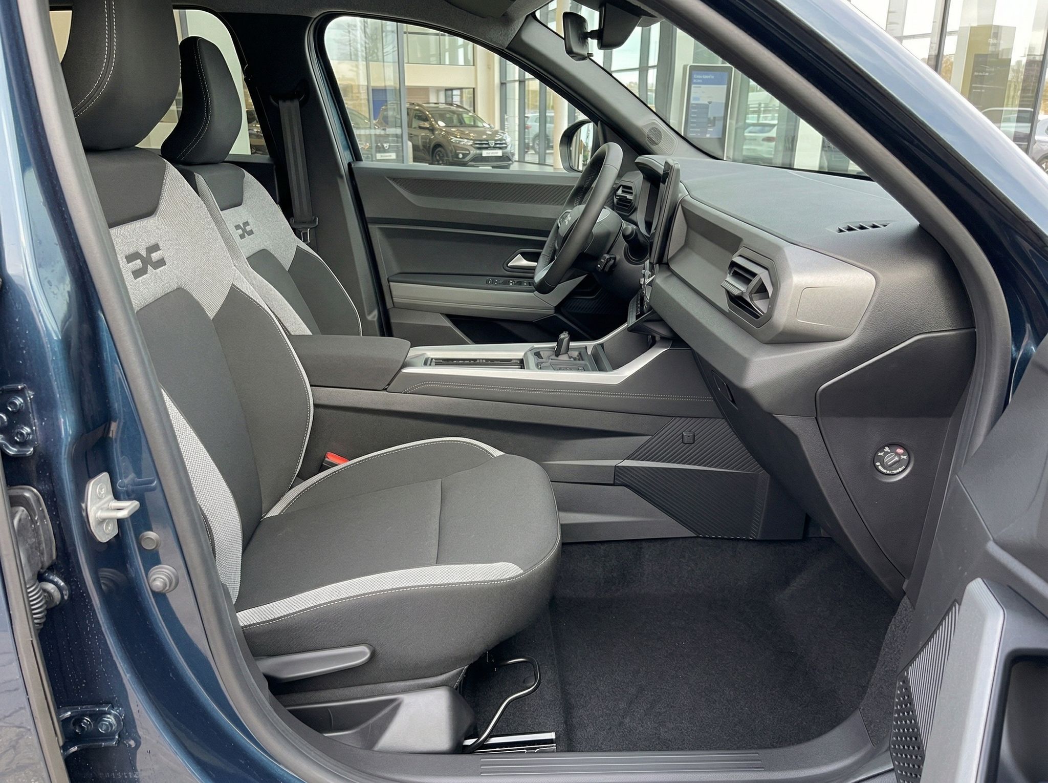 Dacia Fahrzeuginnenraum mit Vordersitzen, Armaturenbrett und Blick in Autohaus-Showroom