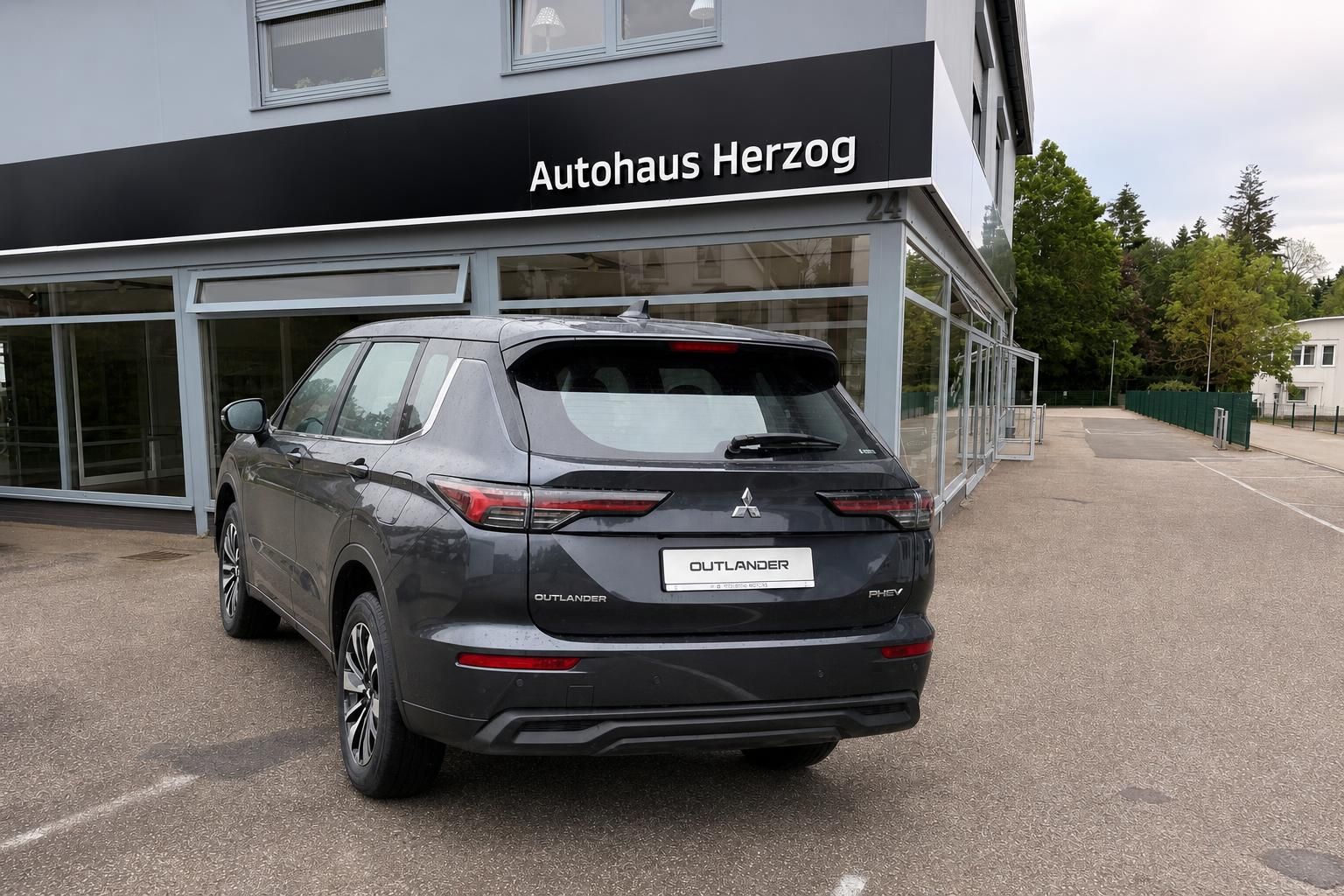 Mitsubishi Outlander PHEV in Grau, Heckansicht vor Autohaus Herzog