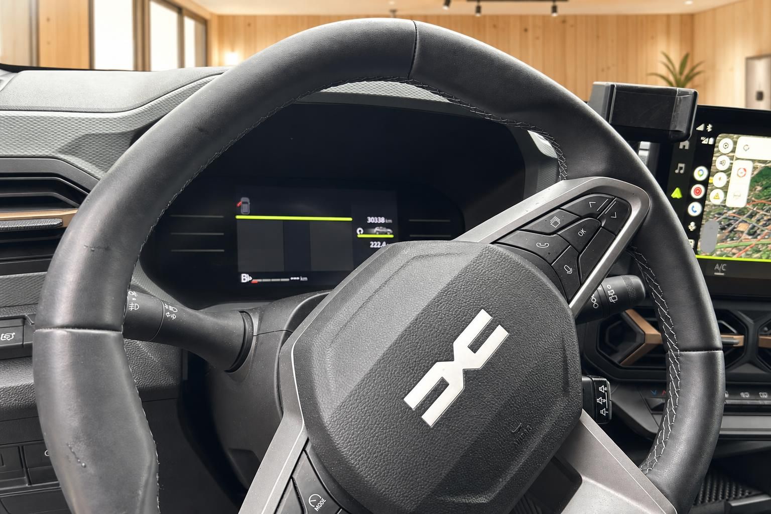 Detailaufnahme Lenkrad mit Markenlogo, digitales Kombiinstrument und Infotainment-Bildschirm im Hintergrund
