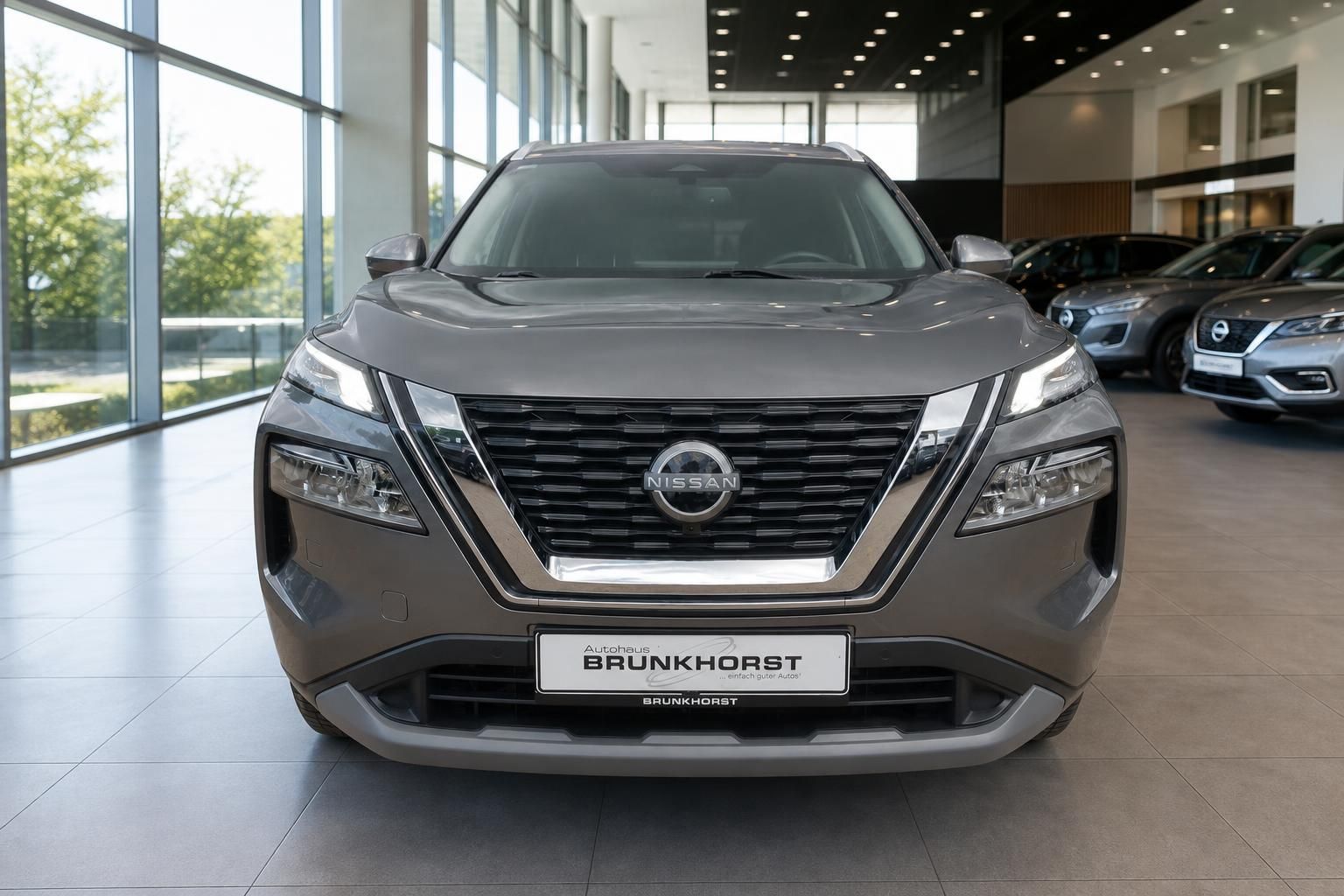 Nissan X-Trail Frontansicht grau mit V-Motion-Kühlergrill und LED-Scheinwerfern im Showroom