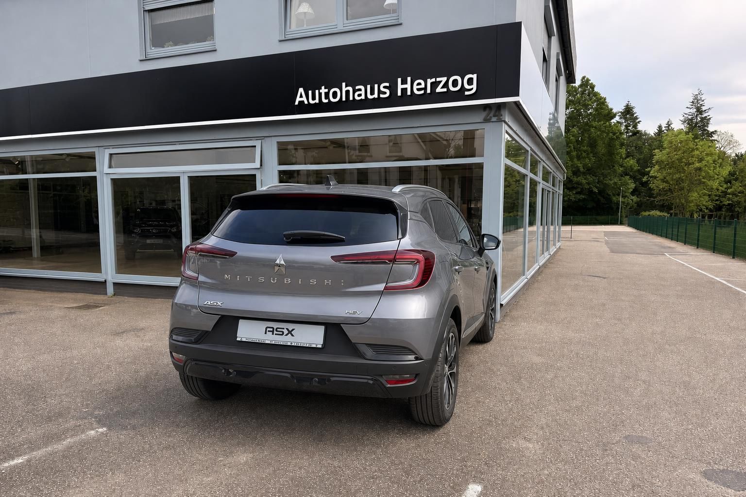Mitsubishi ASX HEV grau Heckansicht gerade vor Autohaus Herzog – Hybrid-SUV Neufahrzeug