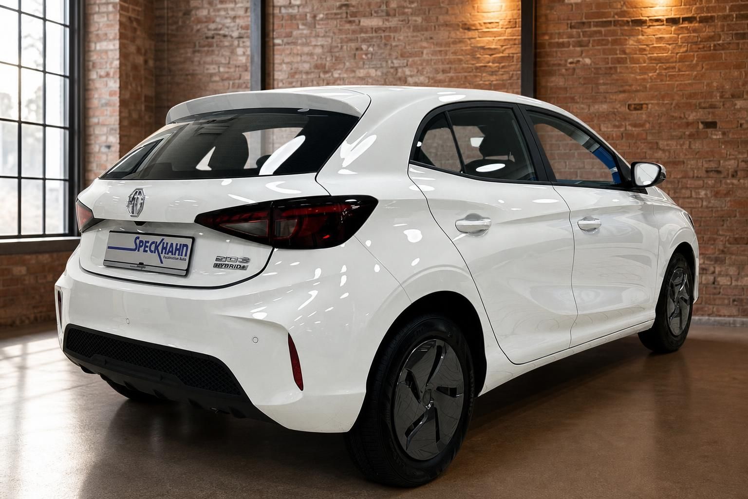 MG3 Hybrid+ weiß, Heck-Seitenansicht vor rustikaler Backsteinwand