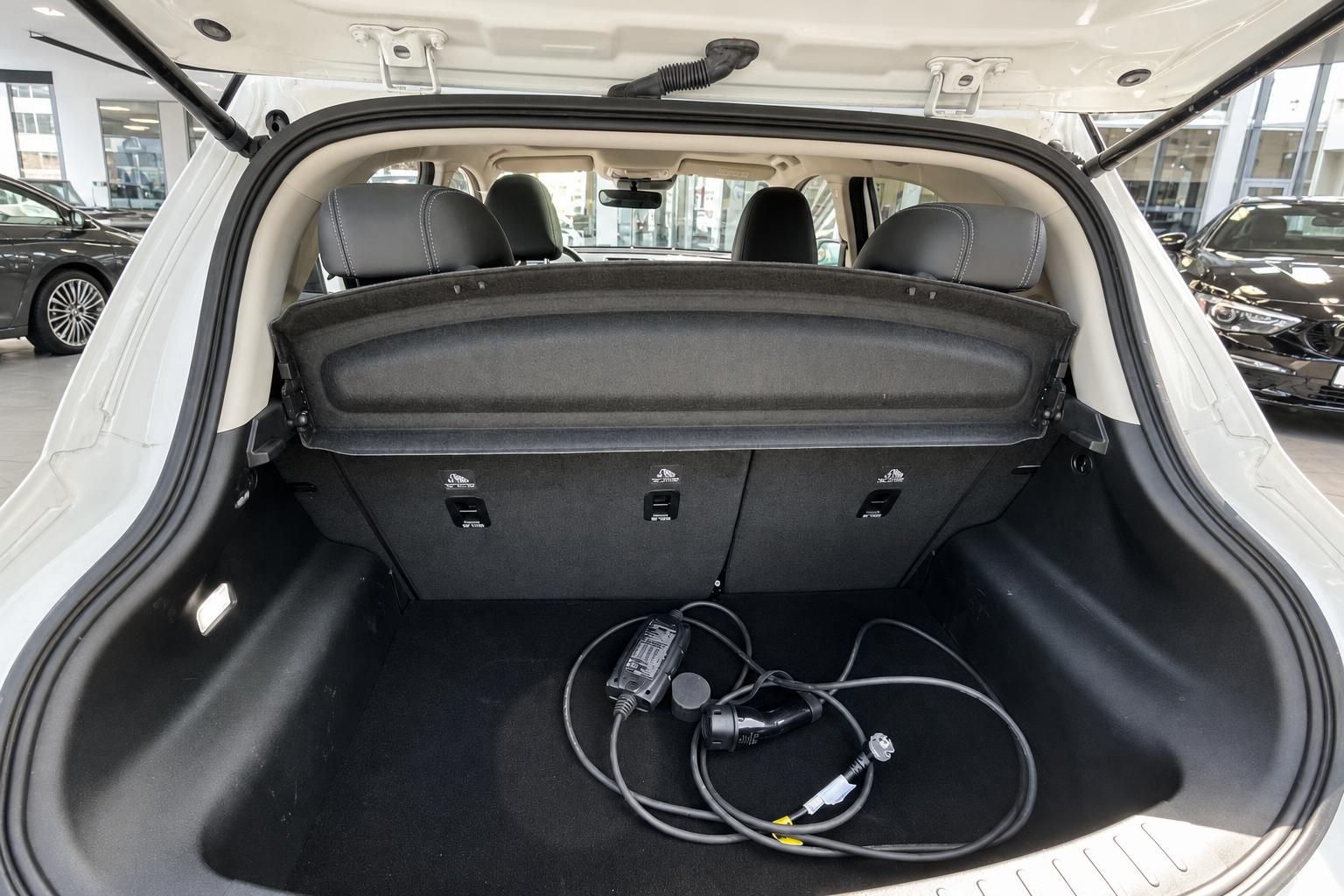 Kofferraum eines weißen Fahrzeugs mit Ladekabel und umklappbaren Rücksitzen im Autohaus