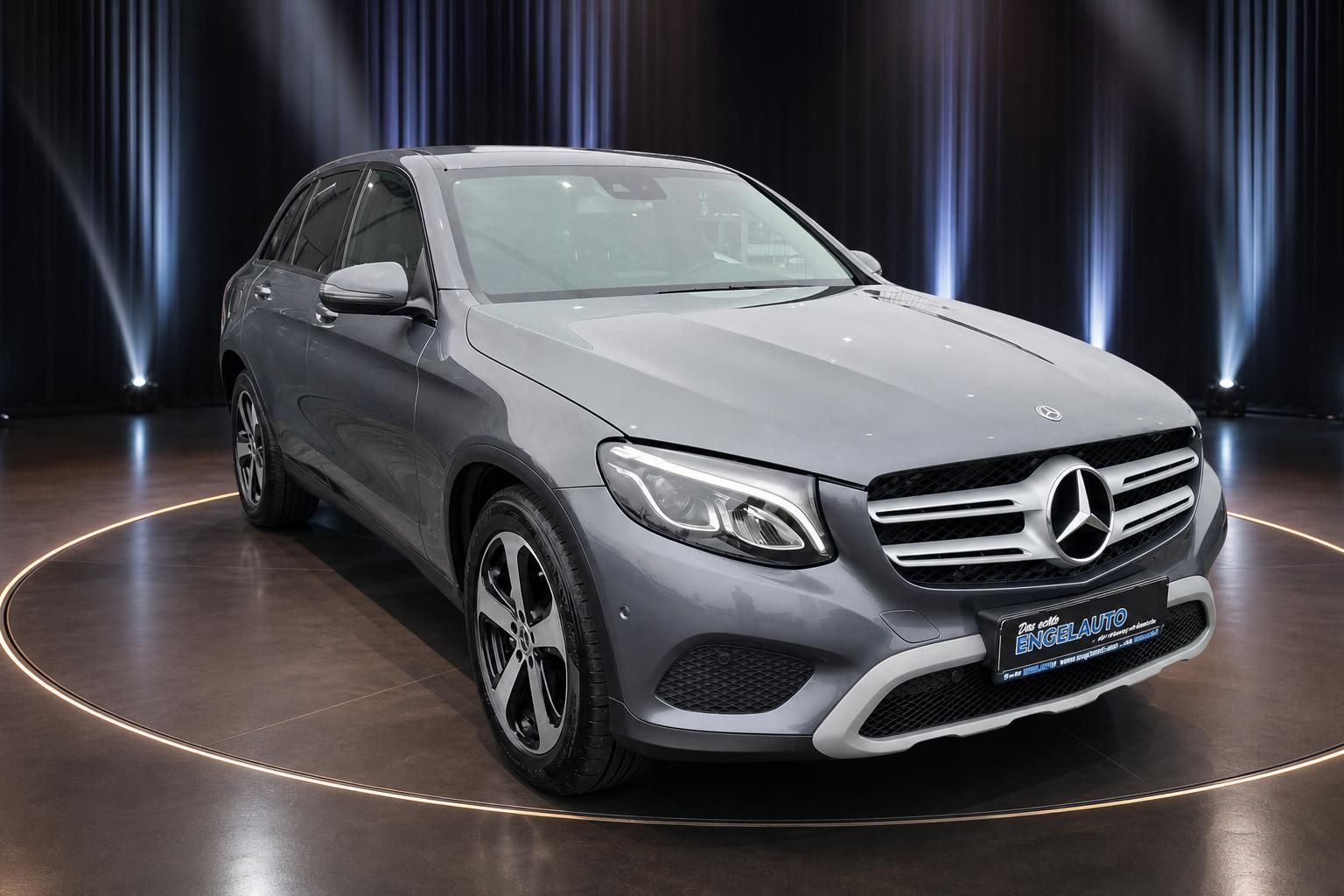 Mercedes GLC SUV grau - Frontansicht schräg links im beleuchteten Autohaus Showroom
