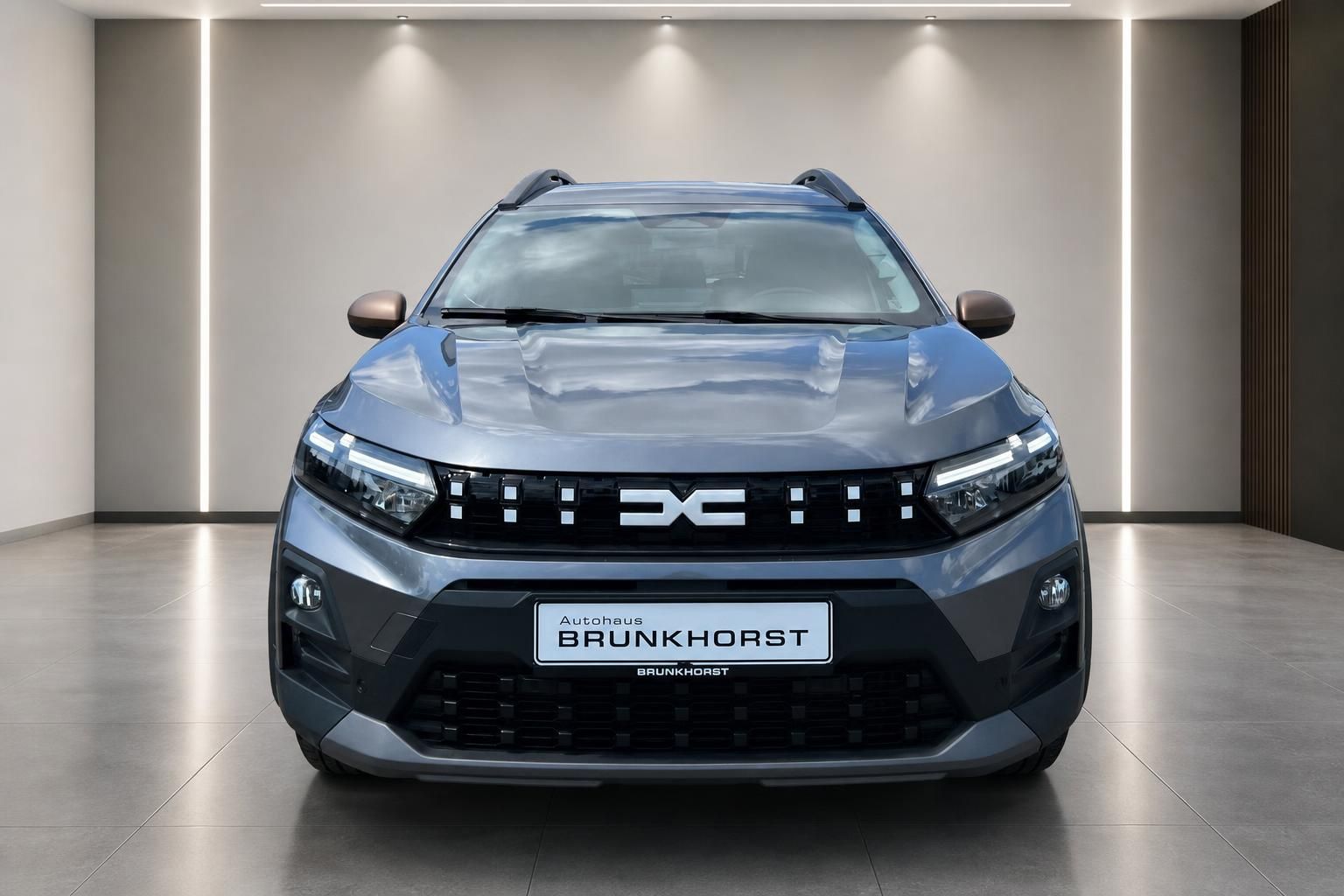 Dacia Fahrzeug Frontansicht grau metallic mit charakteristischem Kühlergrill im Showroom
