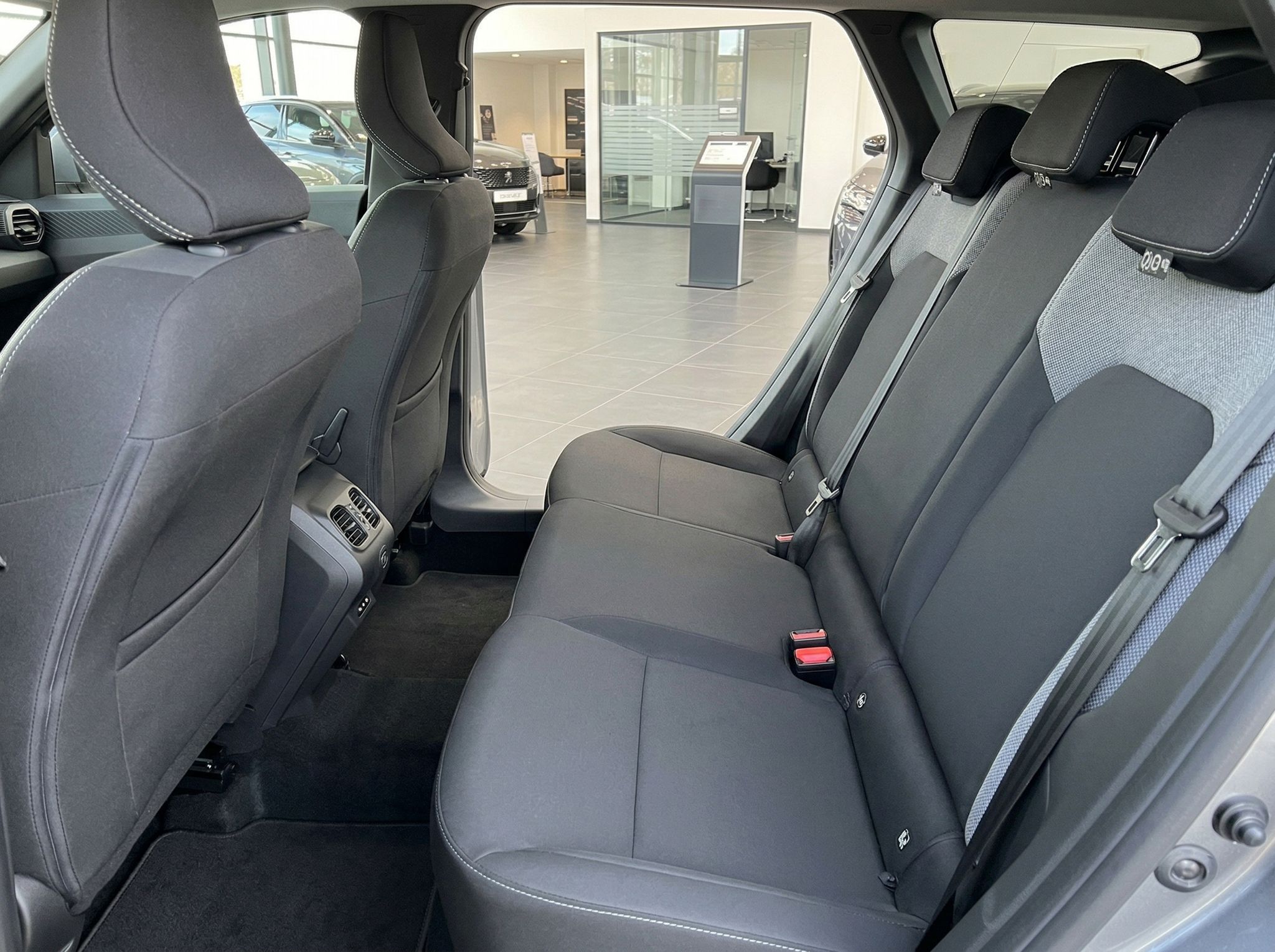 Fahrzeug Rücksitzbank mit grauen Stoffsitzen und Blick durch offene Tür ins Autohaus
