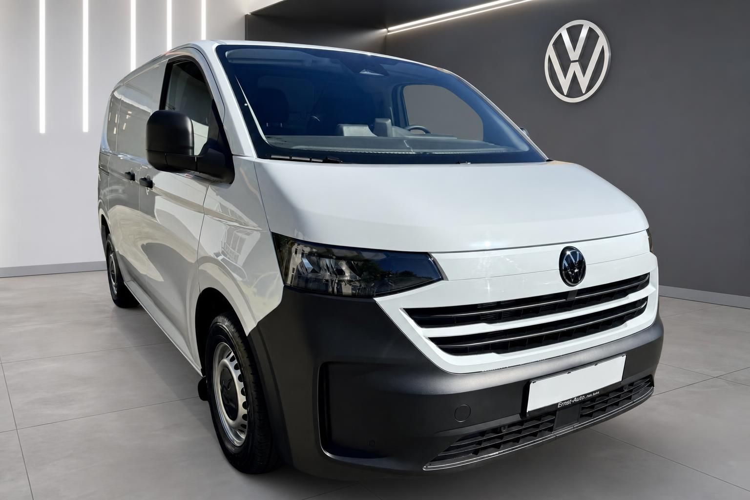 VW Transporter weiß Frontansicht vor VW Logo