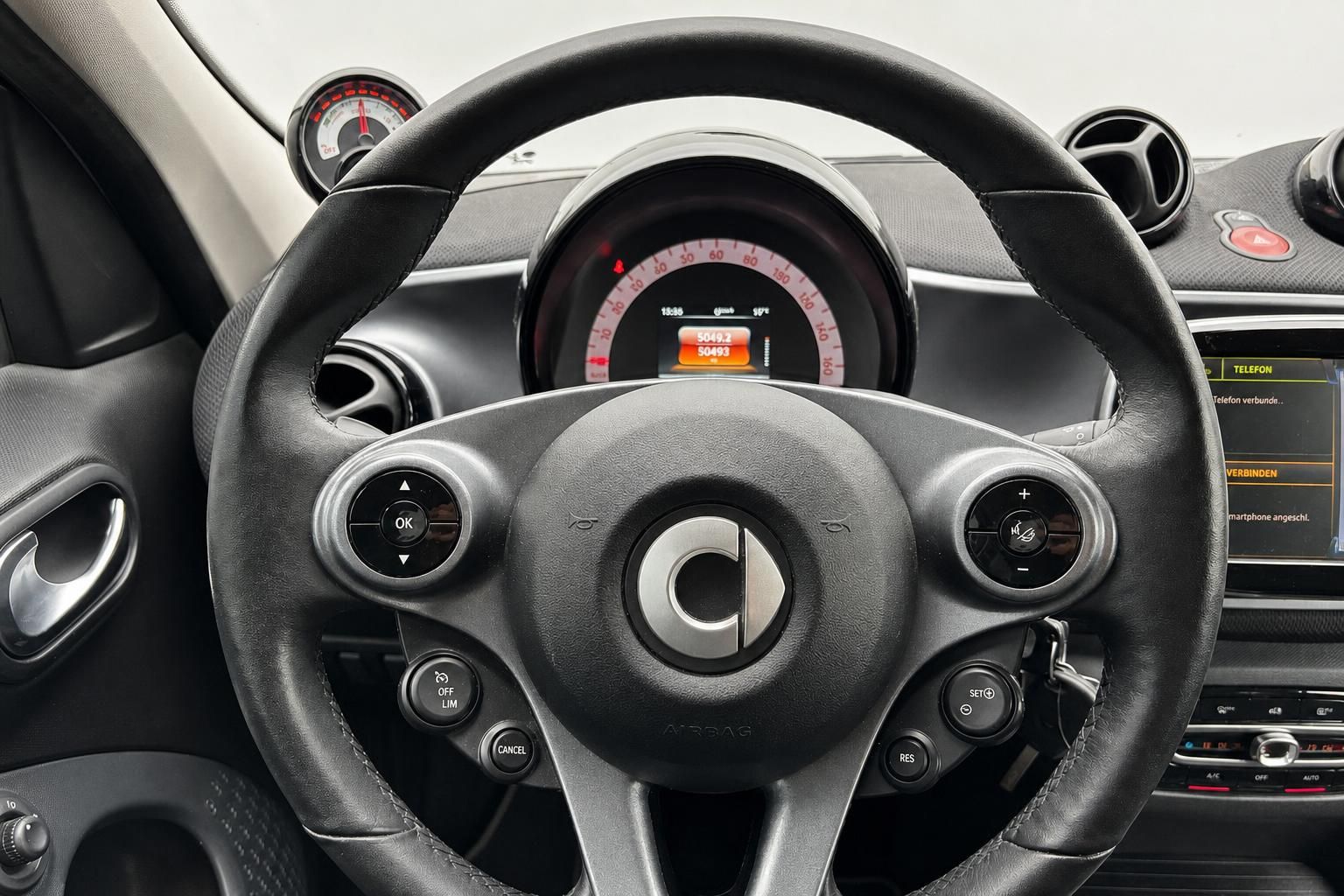 Smart Fortwo Lenkrad mit Multifunktionstasten, Tacho und Infotainment-Display im Hintergrund