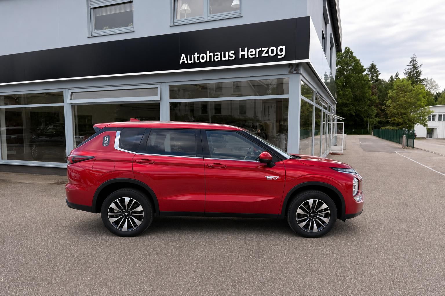 Roter Mitsubishi SUV Seitenansicht vor Autohaus Herzog - modernes Elektro-Fahrzeug mit schwarzen Felgen