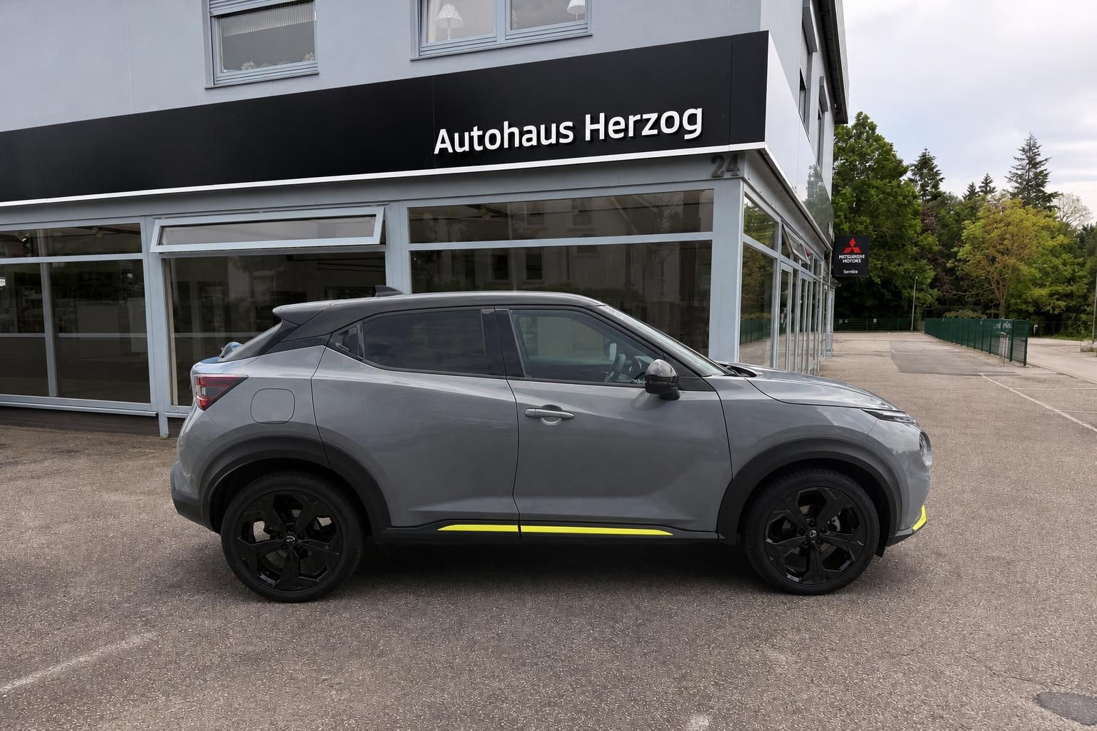 Nissan Juke grau Seitenansicht mit schwarzen Felgen und gelben Akzenten vor Autohaus