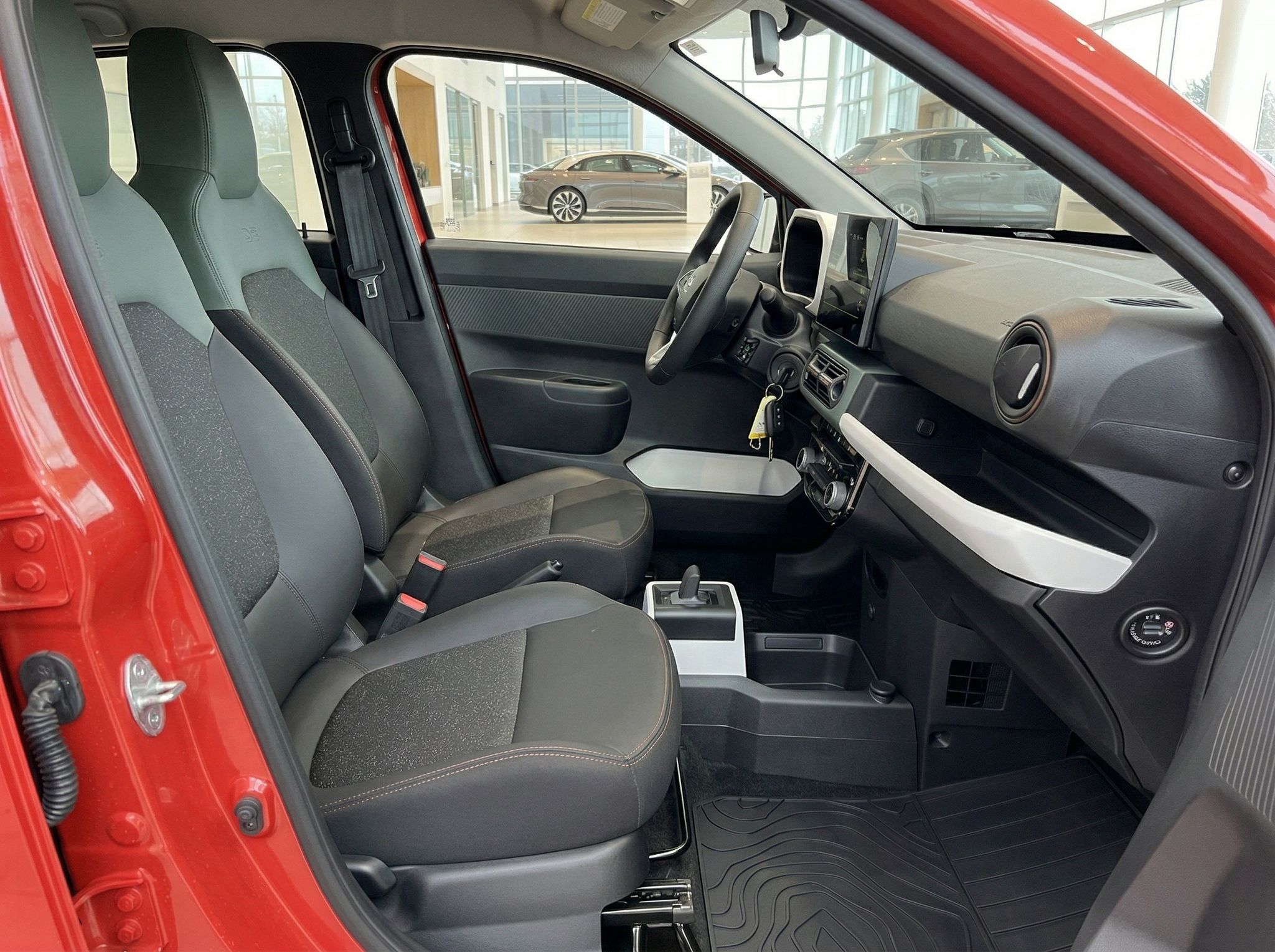 Fahrzeug-Innenraum mit grauen Sitzen, Mittelkonsole und Blick durch offene Beifahrertür