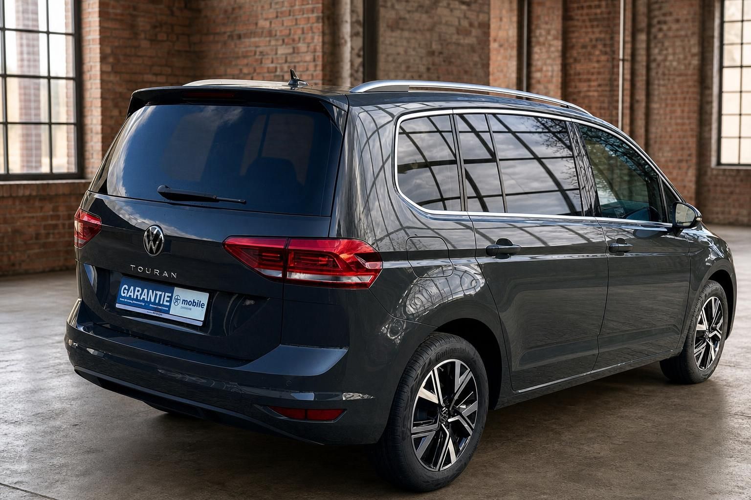 VW Touran dunkelgrau Heckansicht seitlich mit Panorama-Fensterreflexion
