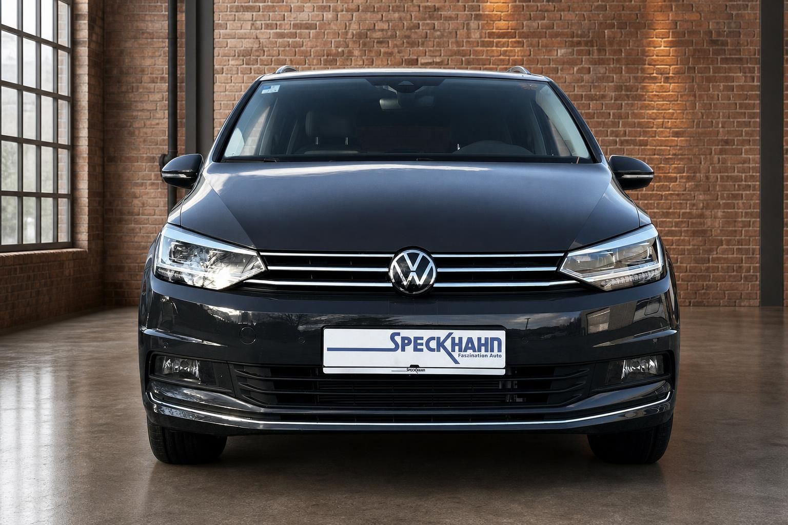 VW Touran Frontansicht in Grau-Metallic, geparkt in Loft-Ausstellungsraum