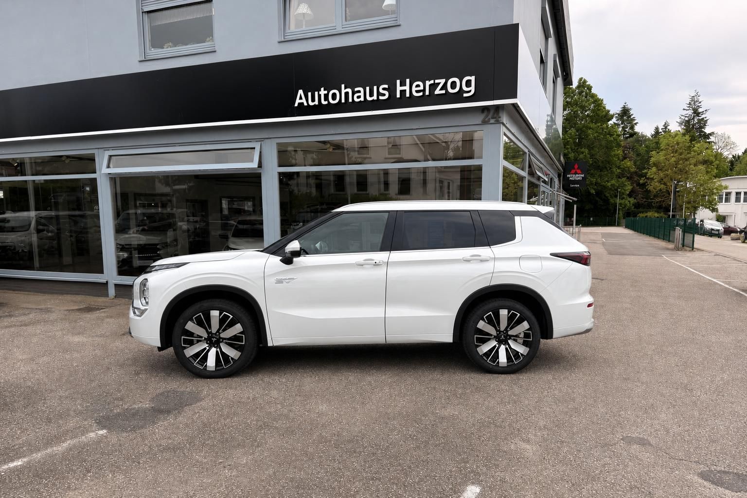Weißer Mitsubishi Outlander SUV Seitenansicht vor Autohaus Herzog - Gebrauchtwagen mit Felgen