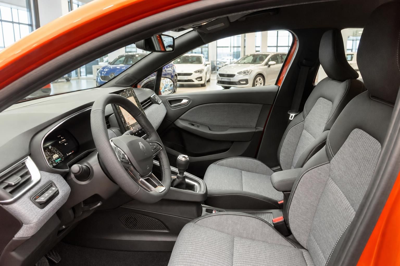 Innenraum eines orangefarbenen Kleinwagens mit Lenkrad, Touchscreen, Schaltgetriebe und grauen Stoffsitzen