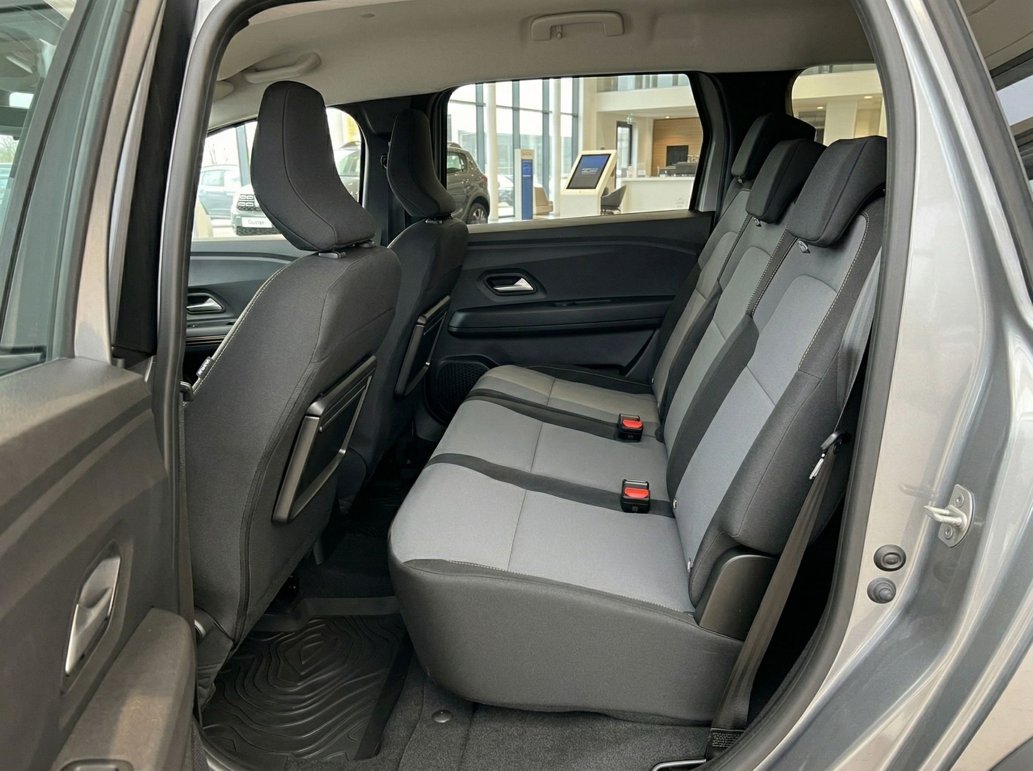 Rücksitzbank eines Fahrzeugs mit grau-schwarzer Polsterung und Sicherheitsgurten