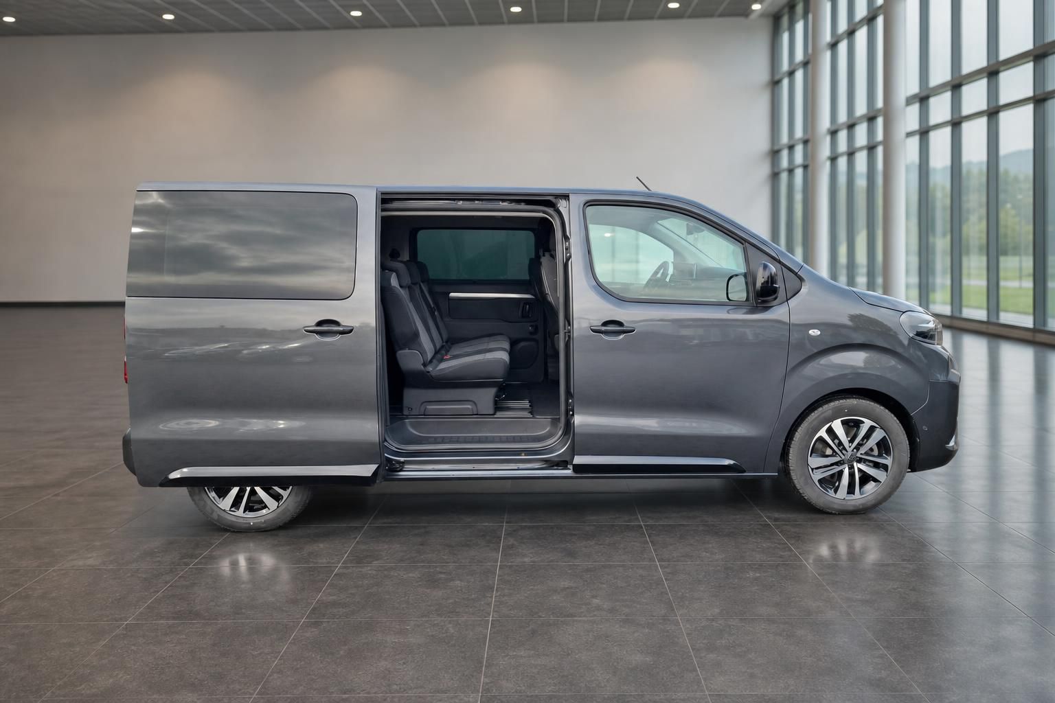 Grauer Peugeot Traveller Van mit geöffneter Schiebetür zeigt Innenraum und Sitze in moderner Ausstellungshalle