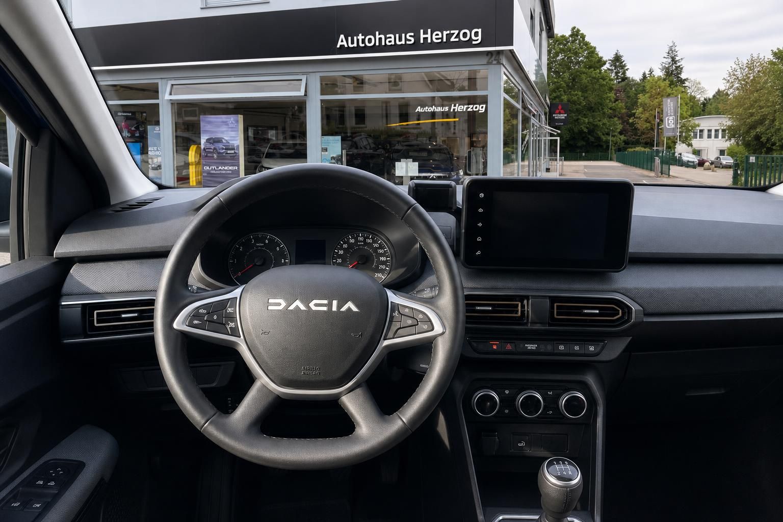 Dacia Cockpit mit Lenkrad, Tacho und Touchscreen-Display vor Autohaus Herzog