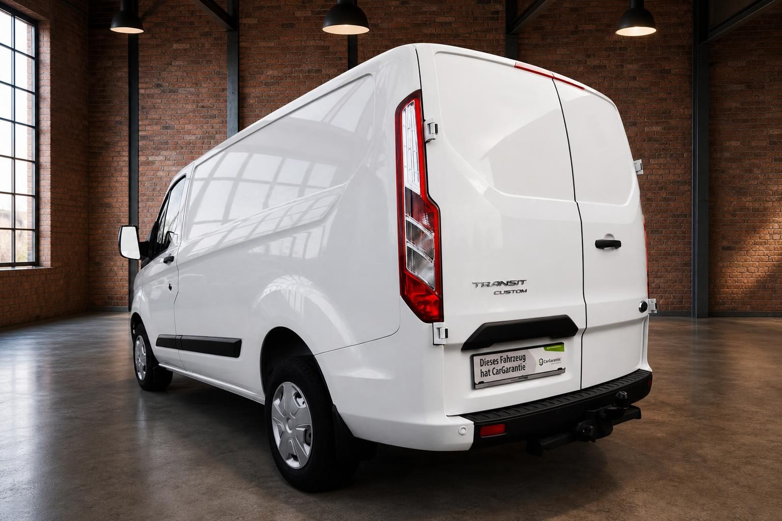 Ford Transit Custom Kastenwagen weiss Heckansicht schraeg links in Industriehalle mit Anhaengerkupplung