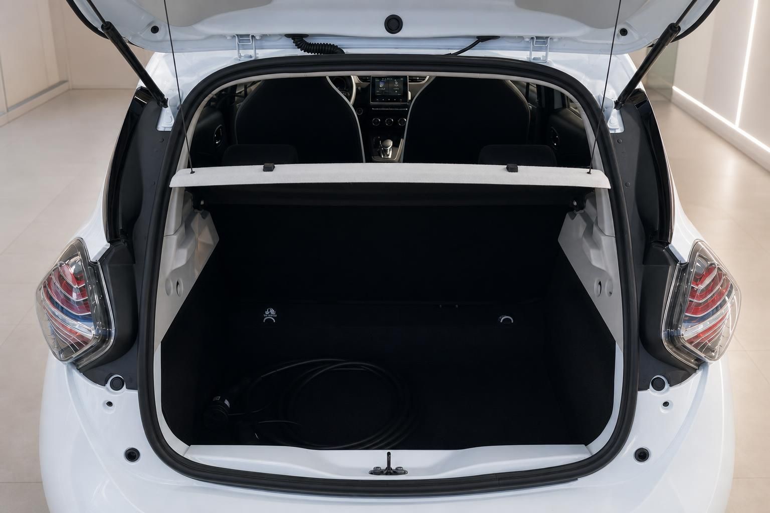 Geöffneter Kofferraum eines weißen Elektroautos mit schwarzer Auskleidung und Ladekabel