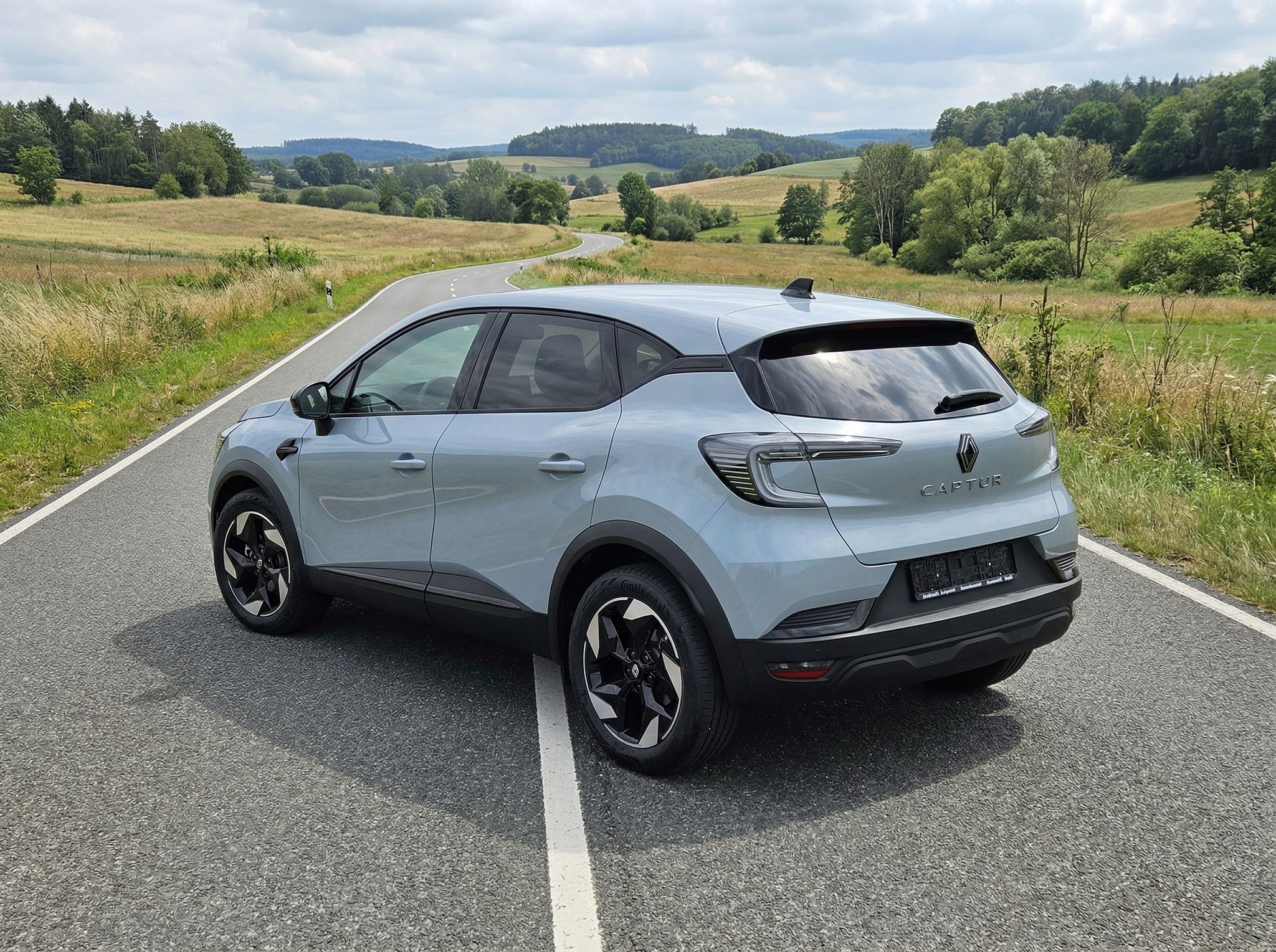 Renault Captur Elektro-SUV silber Heckansicht auf Landstraße in ländlicher Umgebung