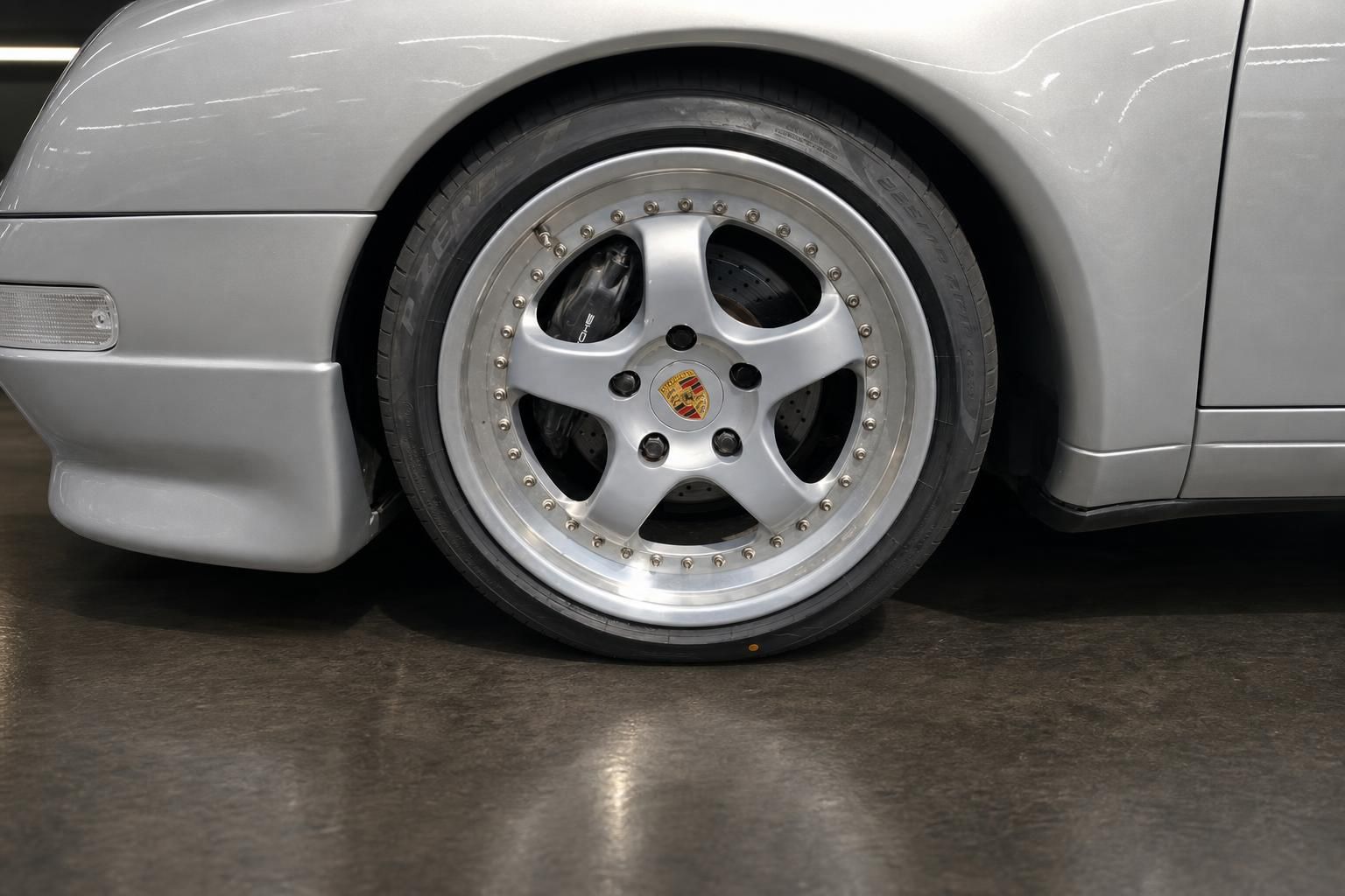 Porsche Felge in Silber mit 5-Speichen-Design und schwarzem Reifen an silbernem Fahrzeug