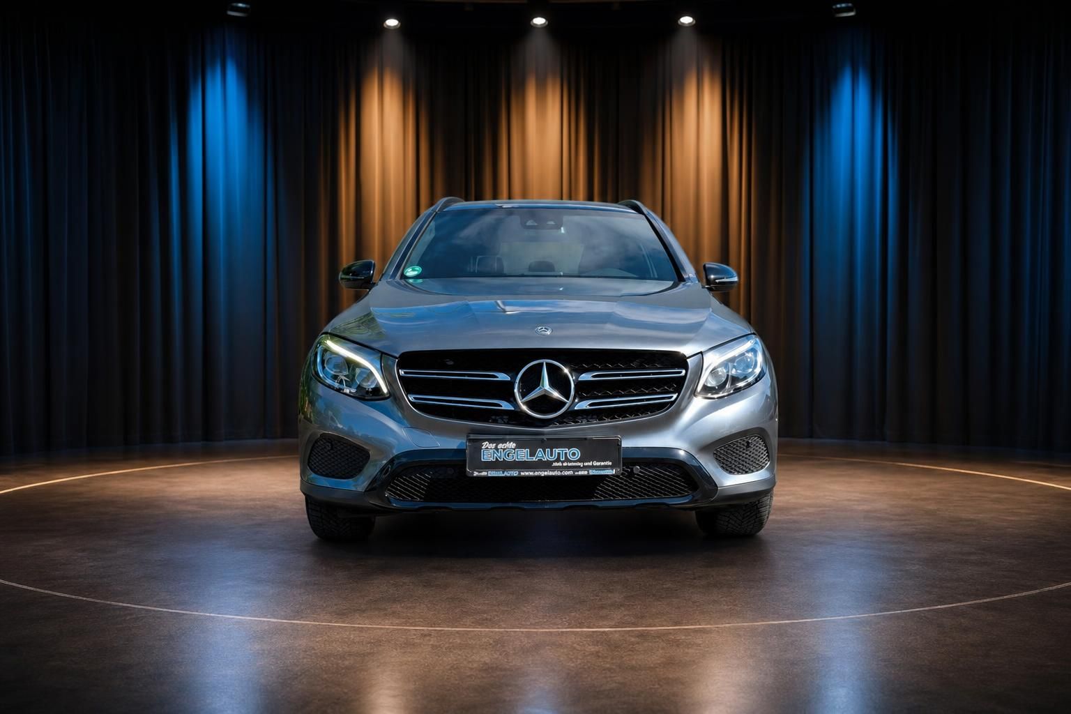 Mercedes GLC SUV in silbergrau, Frontansicht im beleuchteten Showroom mit blau-orangener Kulisse