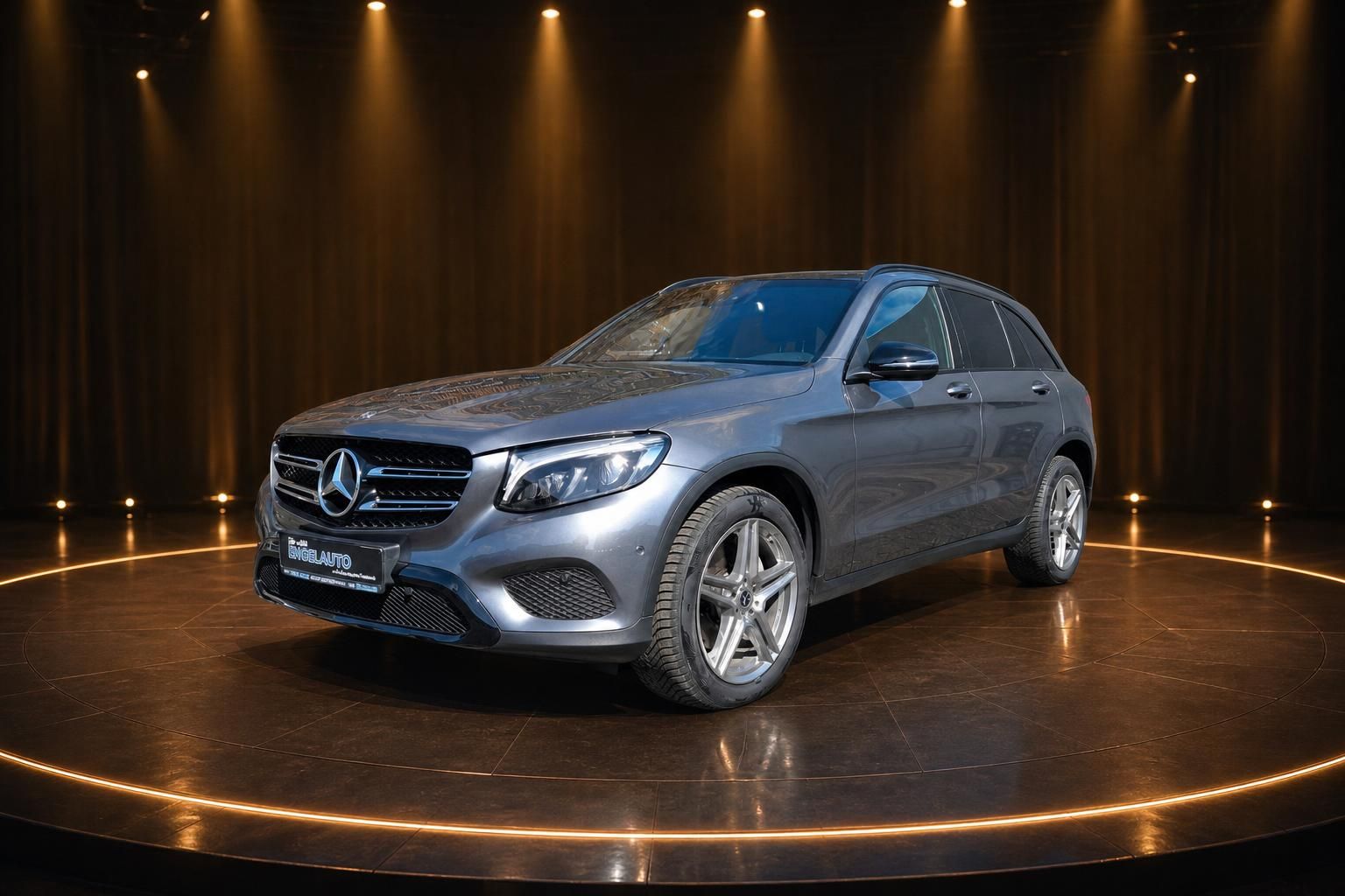 Mercedes GLC SUV silbergrau, Dreiviertelansicht vorne rechts in elegantem Showroom mit Spotlights