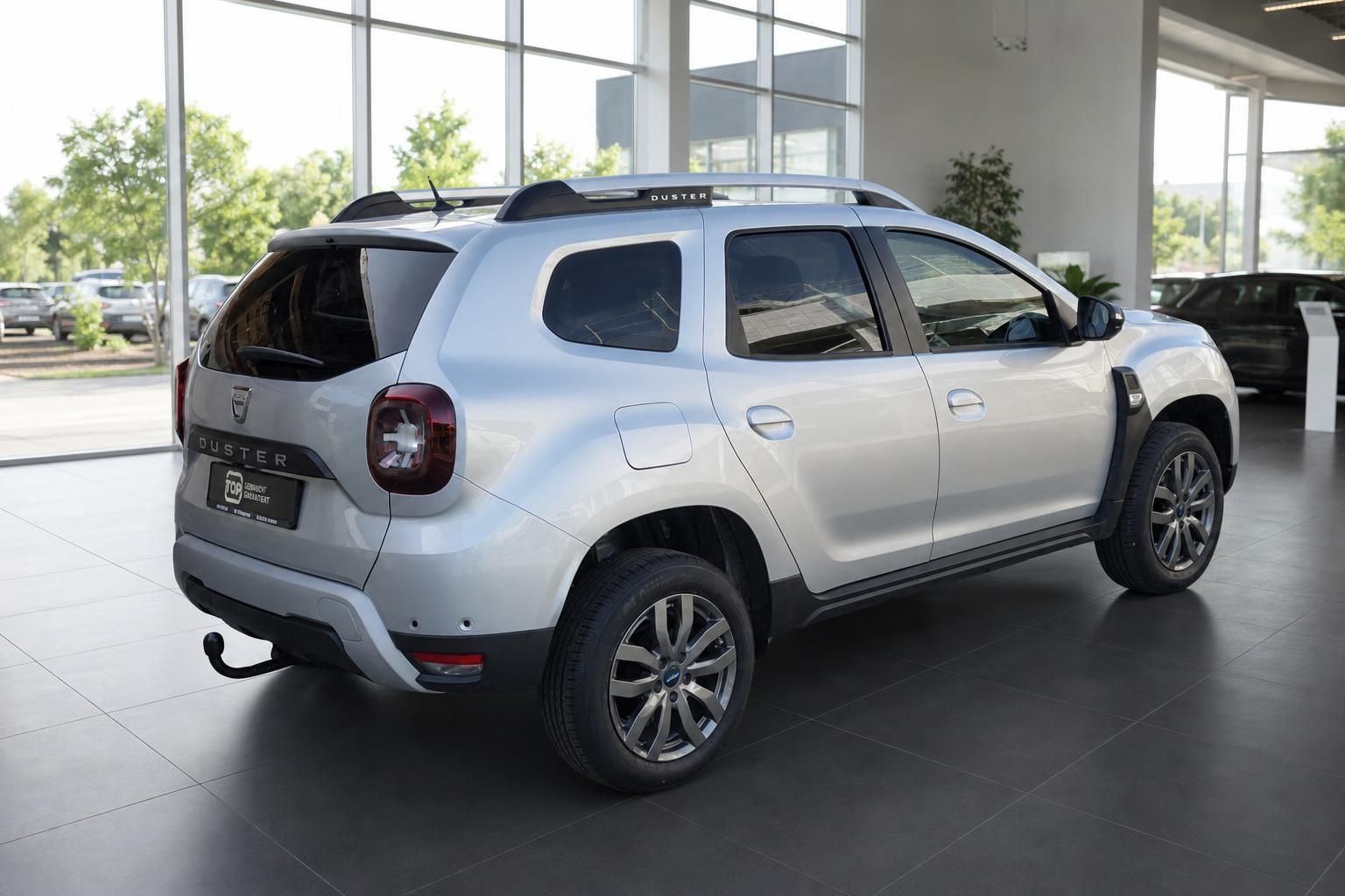 Dacia Duster silber Schrägansicht hinten links mit Anhängerkupplung im Showroom