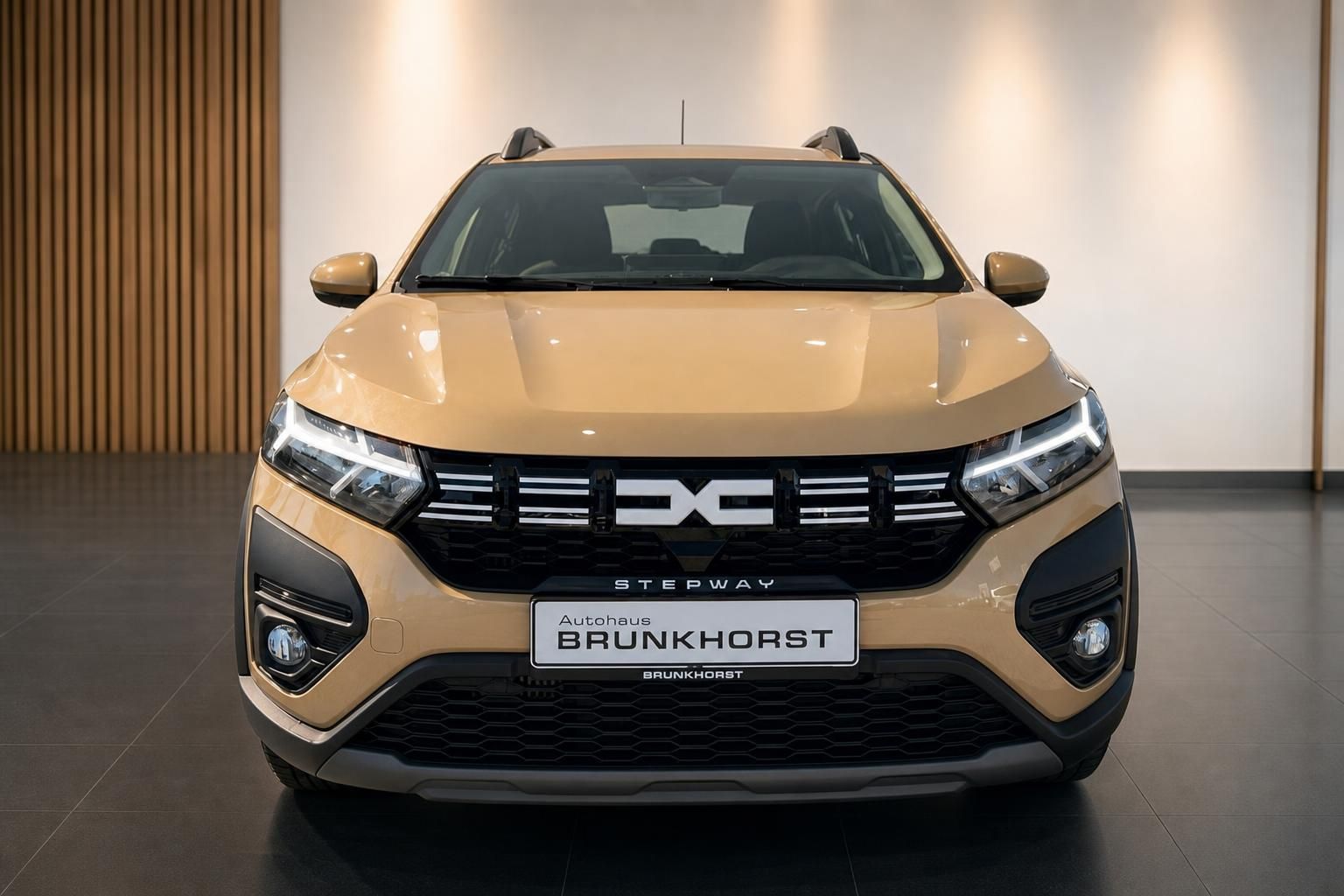 Dacia Sandero Stepway in beige - Frontansicht mit LED-Scheinwerfern im modernen Autohaus-Showroom