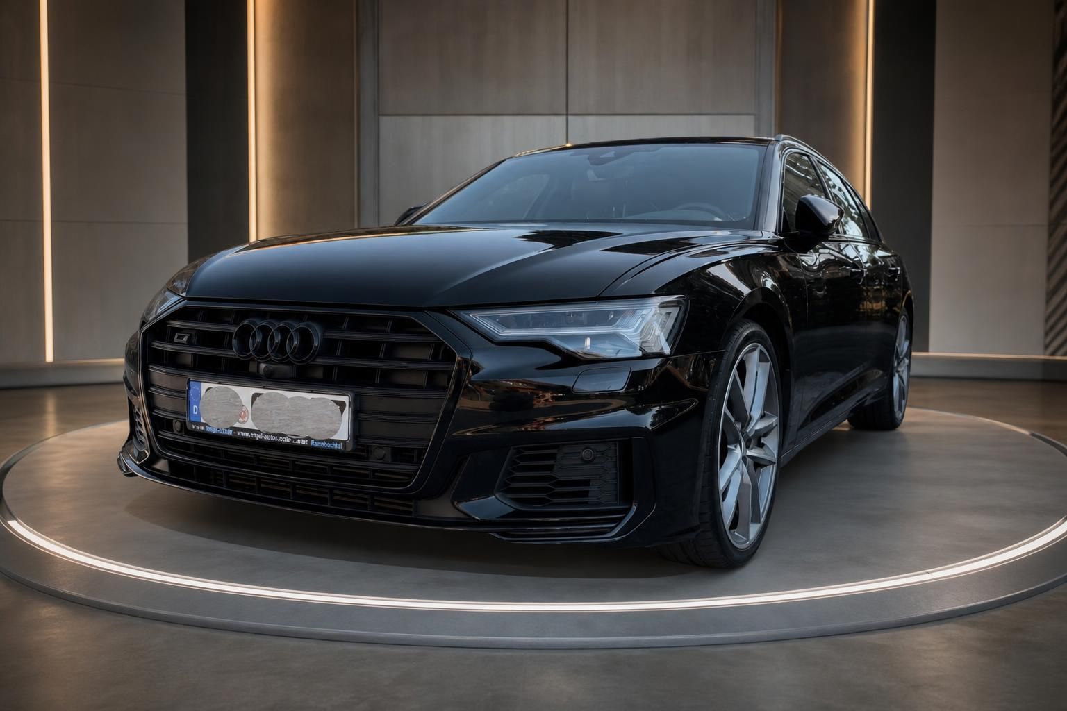 Schwarzer Audi A6 Schrägansicht vorne mit Sportfelgen auf beleuchteter Ausstellungsplattform