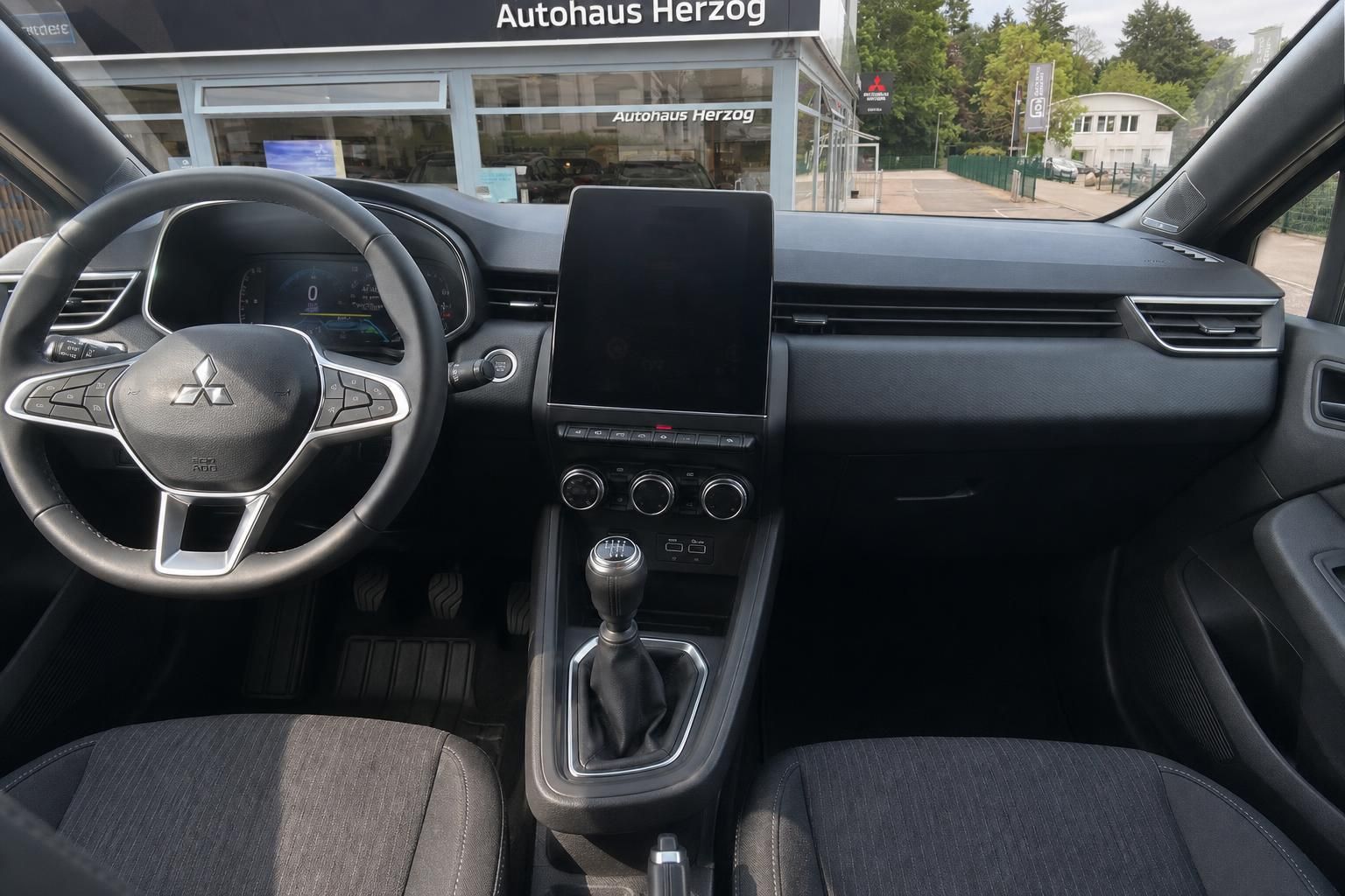 Mitsubishi Innenraum mit Lenkrad, Touchscreen-Display und manueller Schaltung in dunkler Ausstattung
