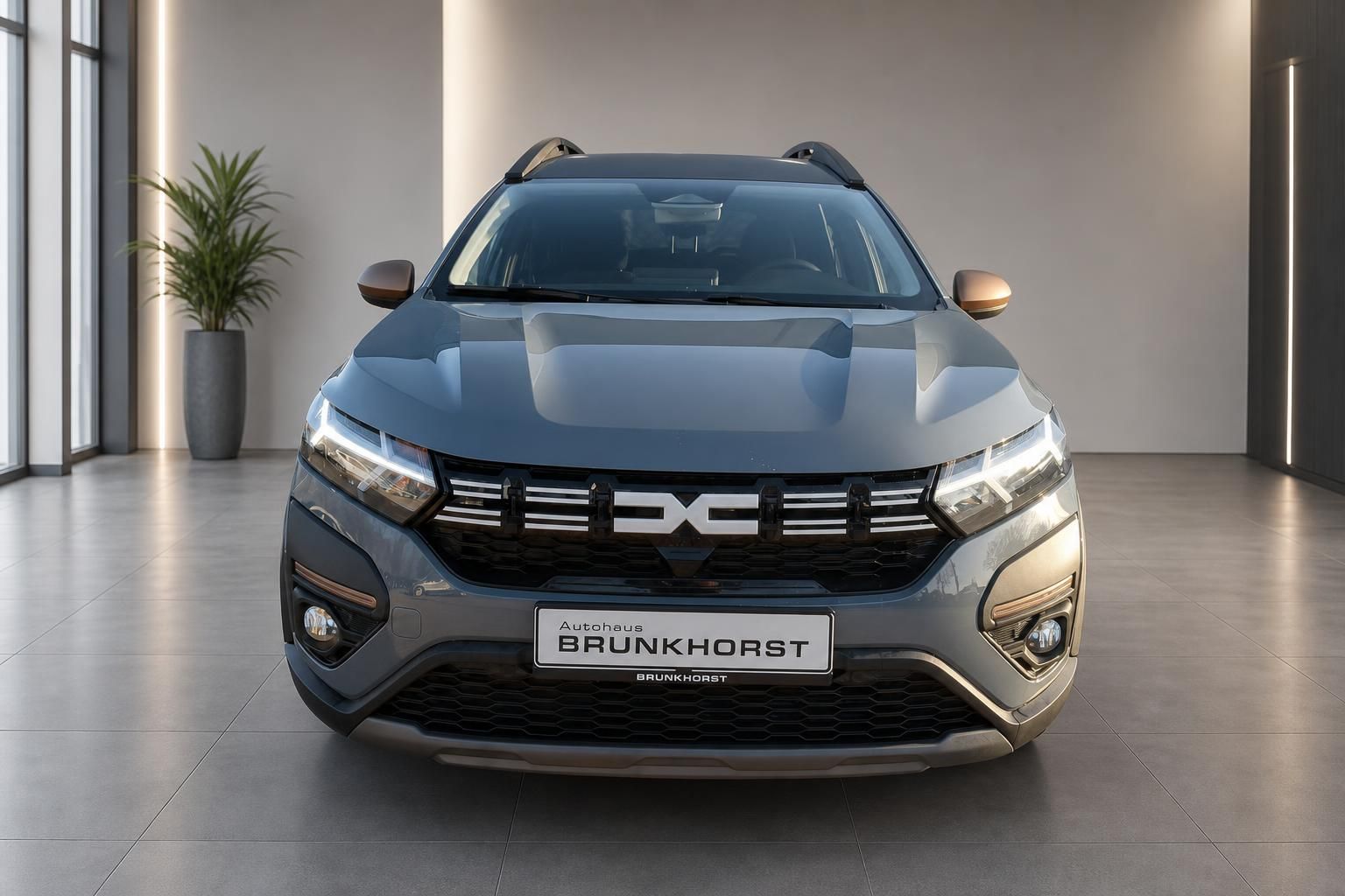 Dacia SUV grau metallic Frontansicht mit Händlerkennzeichen Brunkhorst in modernem Showroom