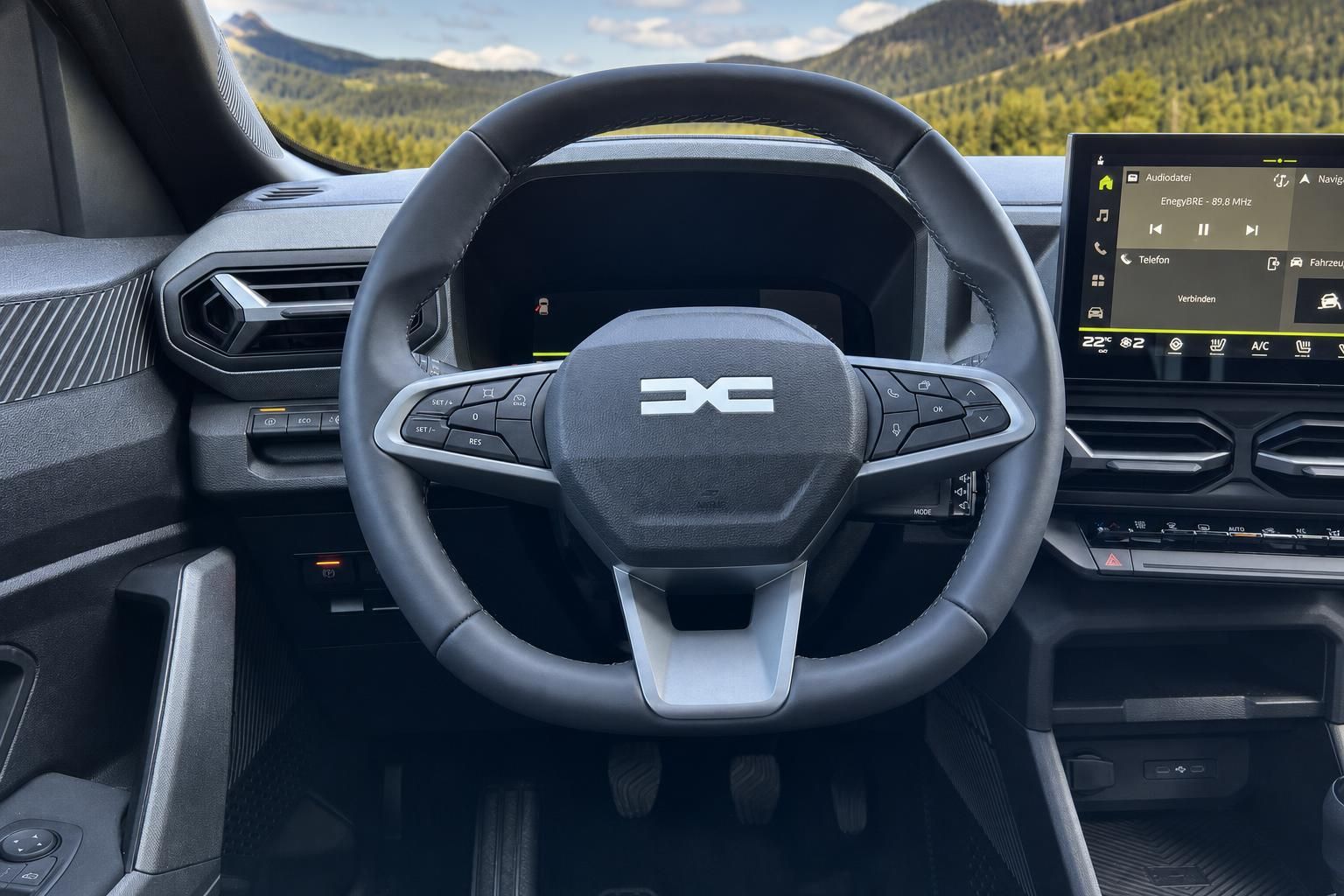 Fahrzeug Cockpit mit Lenkrad und digitalem Infotainment-Display bei Berglandschaft im Hintergrund