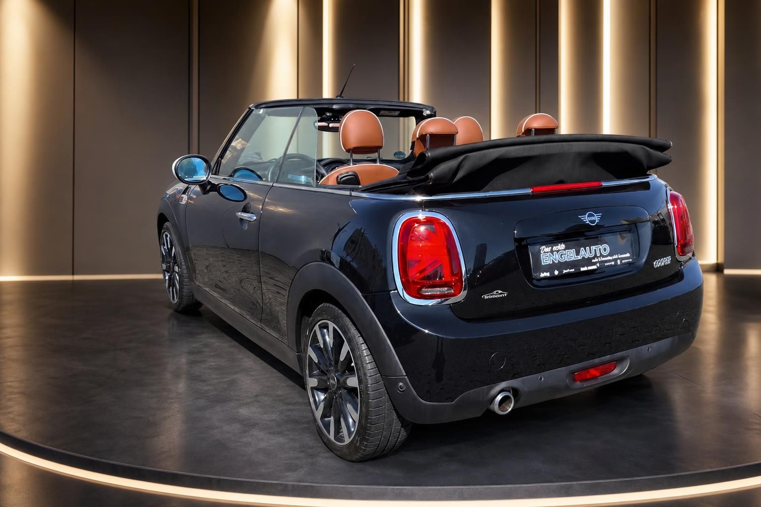 MINI Cooper Cabrio offen schwarz mit orangenen Ledersitzen - Dreiviertel Heckansicht im Showroom