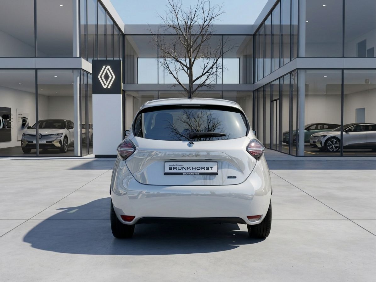 Renault ZOE Heckansicht weiß vor modernem Autohaus mit Glasfassade