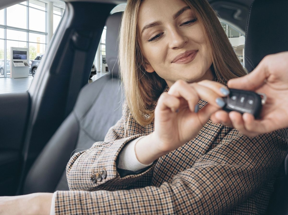 Frau erhält Autoschlüssel im Autohaus – Fahrzeugübergabe im Innenraum