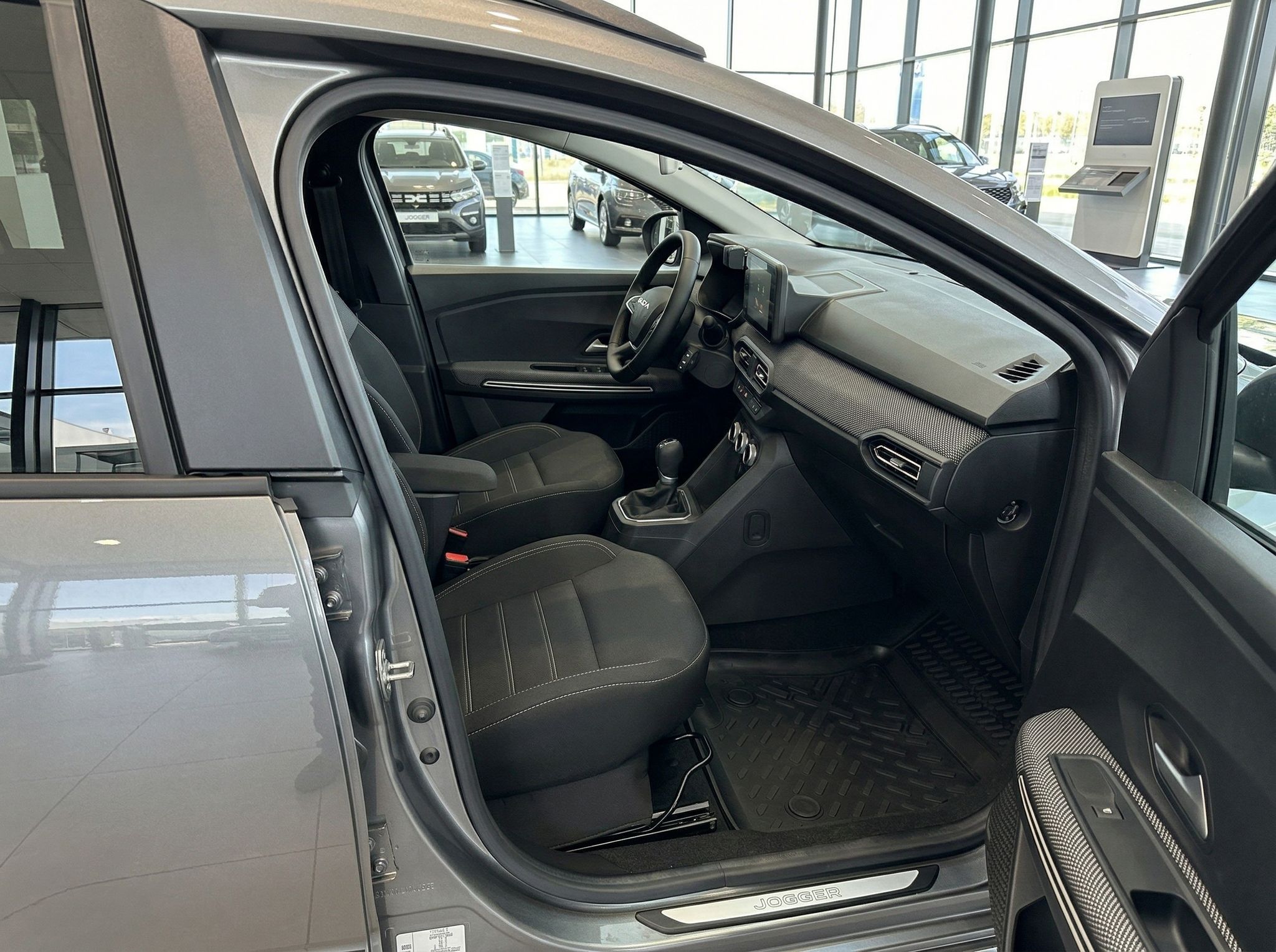 Dacia Innenraum Beifahrerseite mit Sitzen, Armaturenbrett und offener Tür