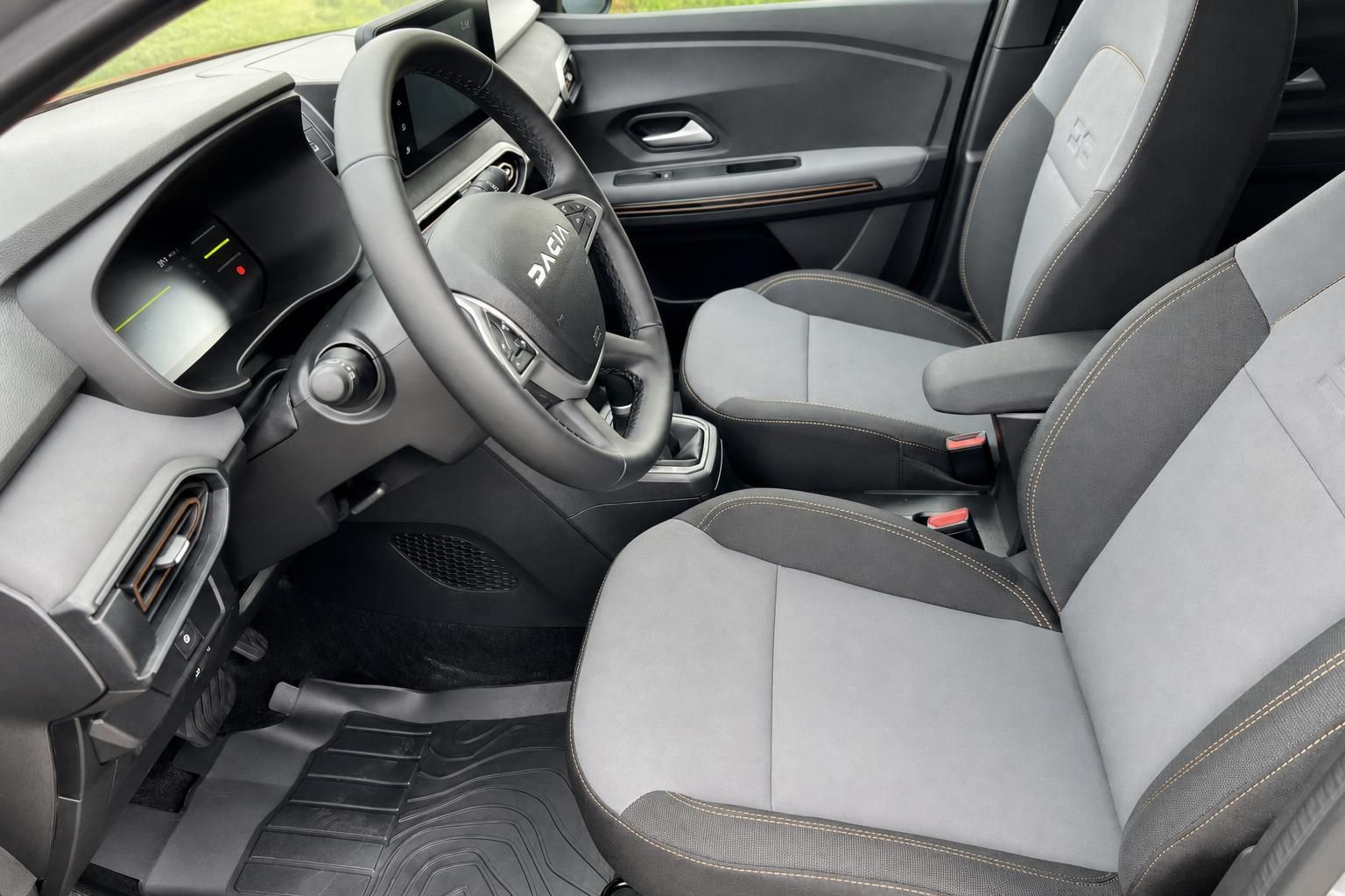 Dacia Fahrersitz und Cockpit mit Lenkrad, Instrumententafel und heller Stoffausstattung