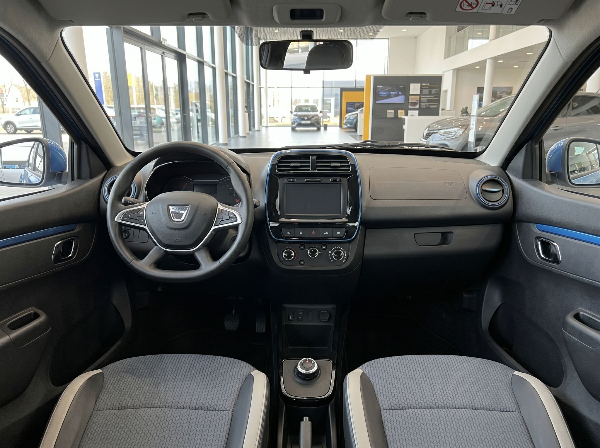 Innenraum eines blauen Dacia Fahrzeugs mit Armaturenbrett, Lenkrad und grauen Sitzen im Autohaus