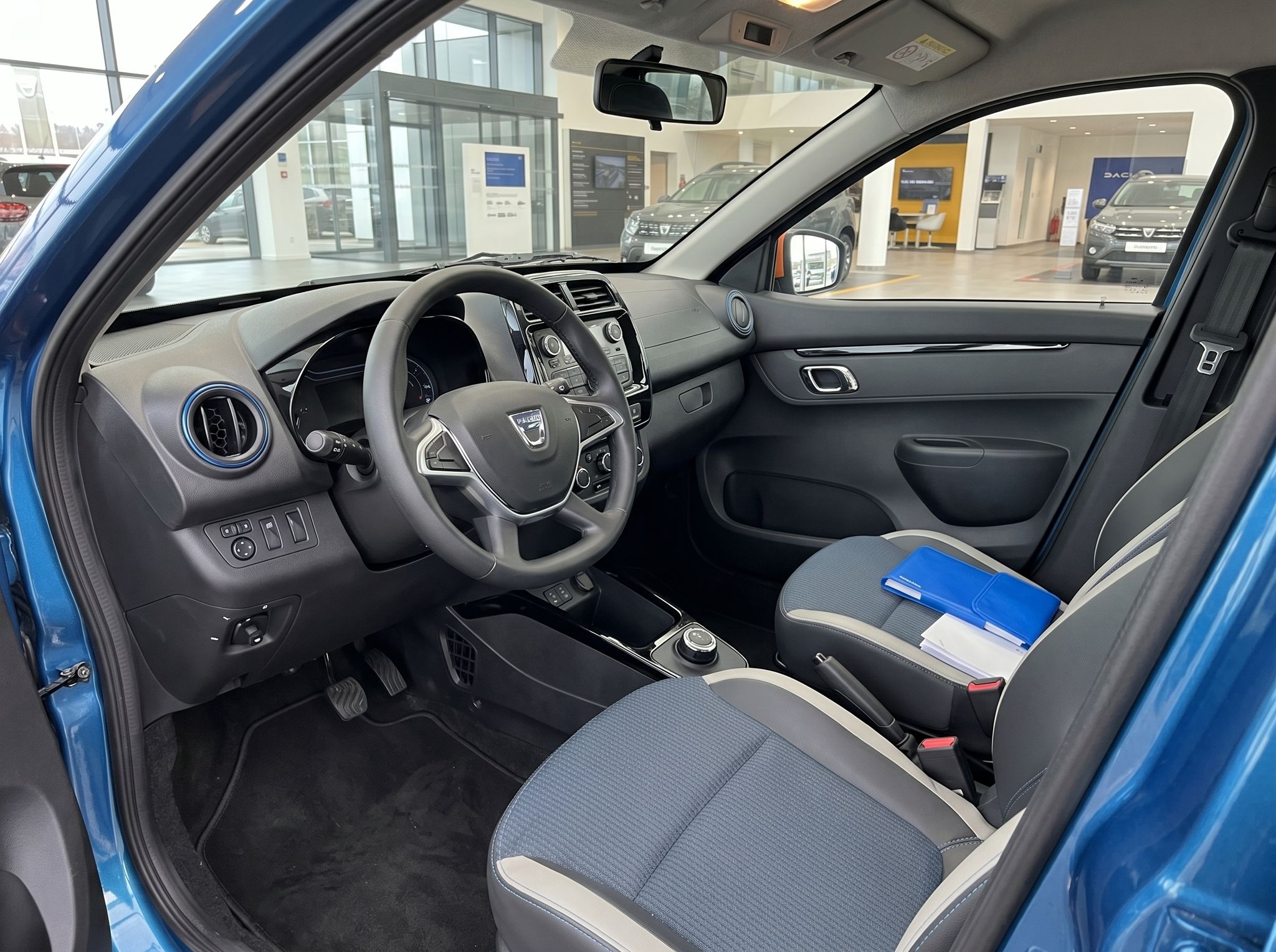 Fahrerbereich eines blauen Dacia mit Lenkrad, Mittelkonsole und grauen Stoffsitzen im Autohaus