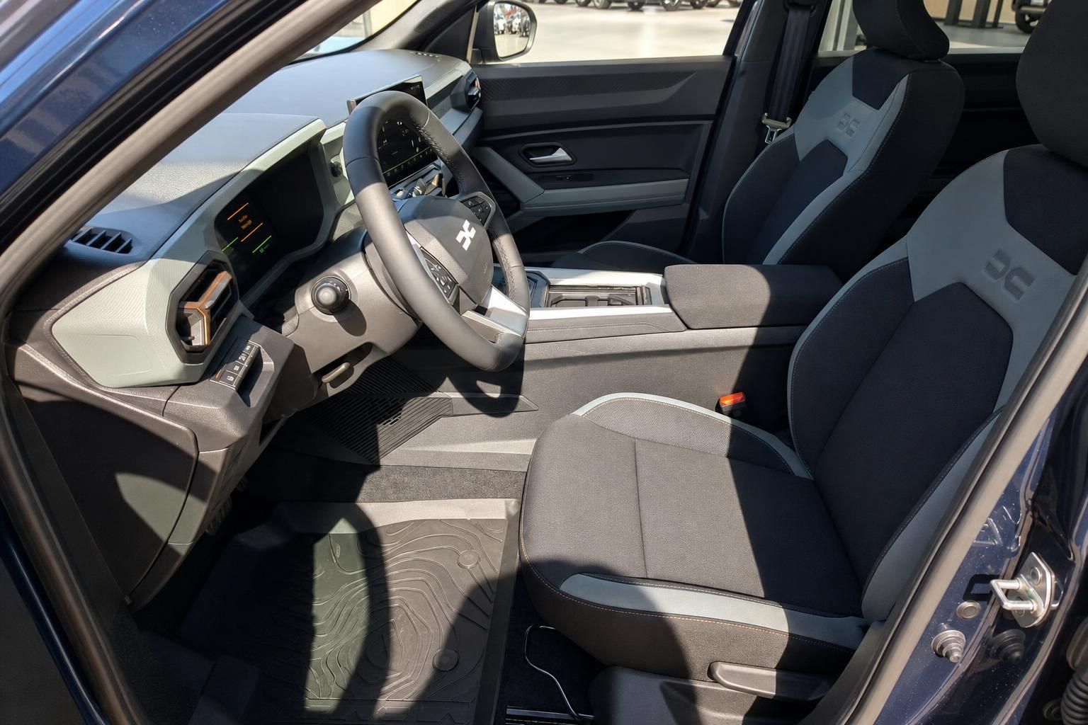 Fahrzeuginnenraum mit beige-schwarzer Ausstattung, Lenkrad und Sitzen bei geöffneter Fahrertür