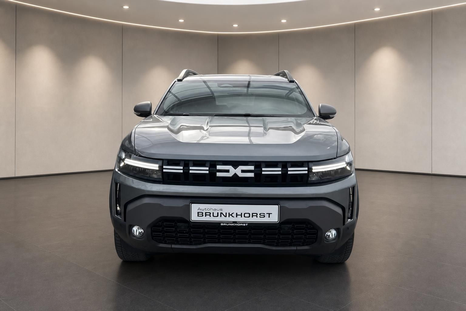 Dacia SUV Frontansicht grau mit LED-Scheinwerfern im modernen Autohaus Showroom
