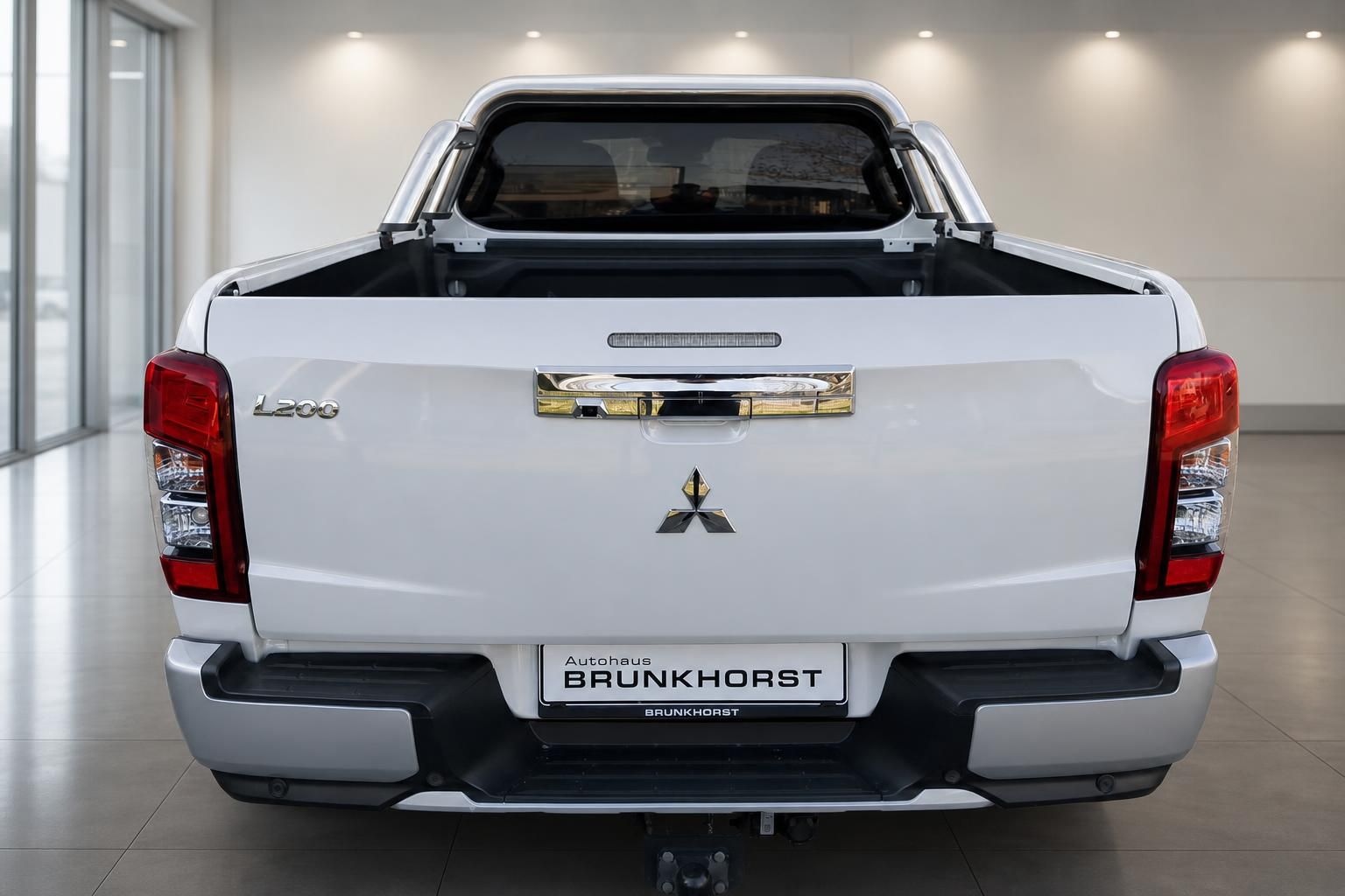 Mitsubishi L200 Pickup weiß von hinten mit Überrollbügel und Händlerkennzeichen im Autohaus