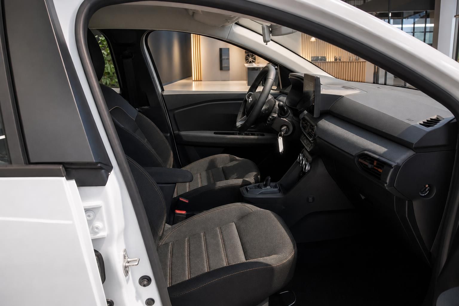 Dacia Innenraum Vordersitze mit dunklem Stoff, orangefarbener Naht und geöffneter Fahrertür