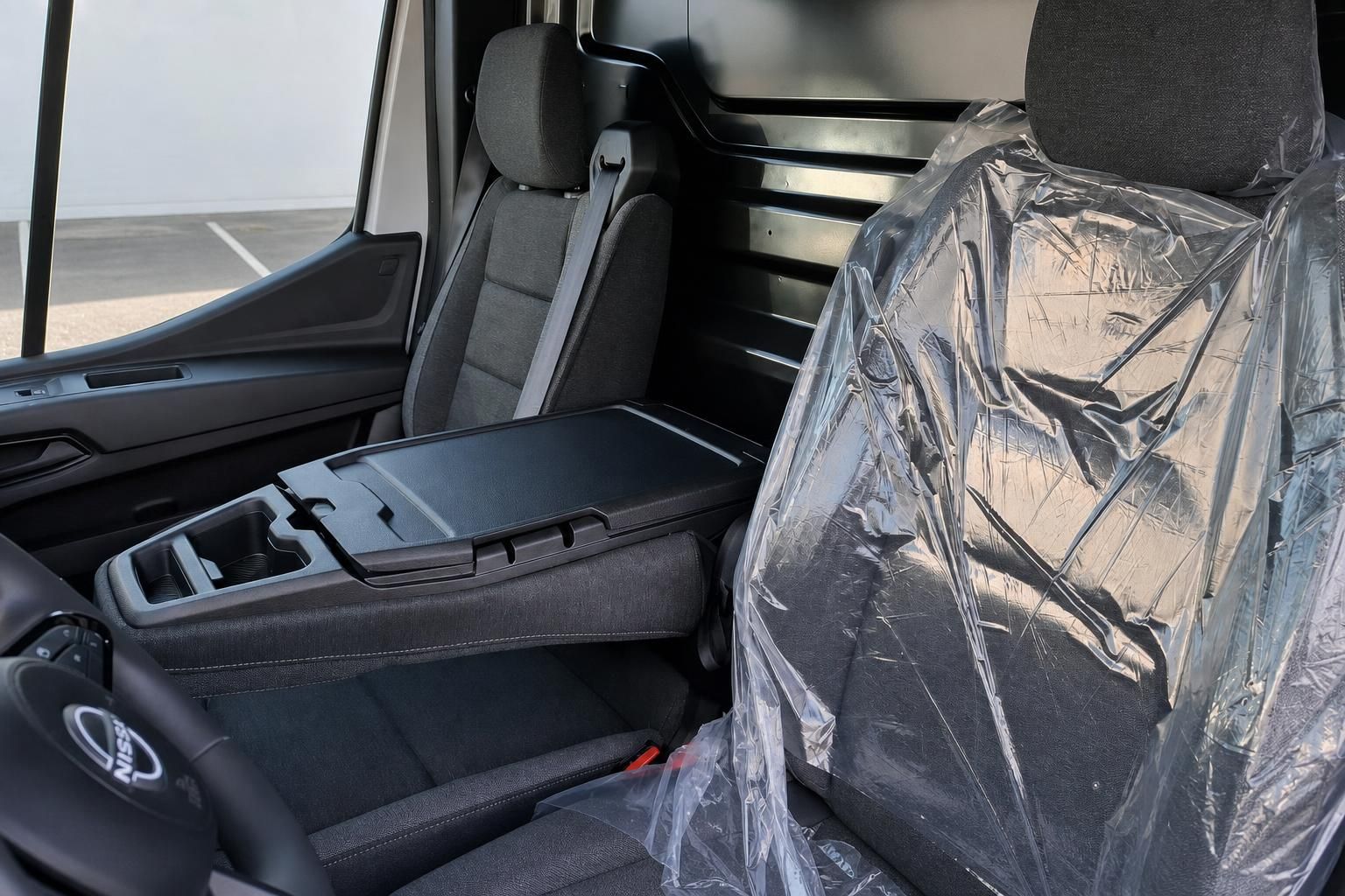 Fahrzeuginnenraum mit schwarzen Sitzen, Mittelkonsole und Plastikschutzfolien im Innenbereich